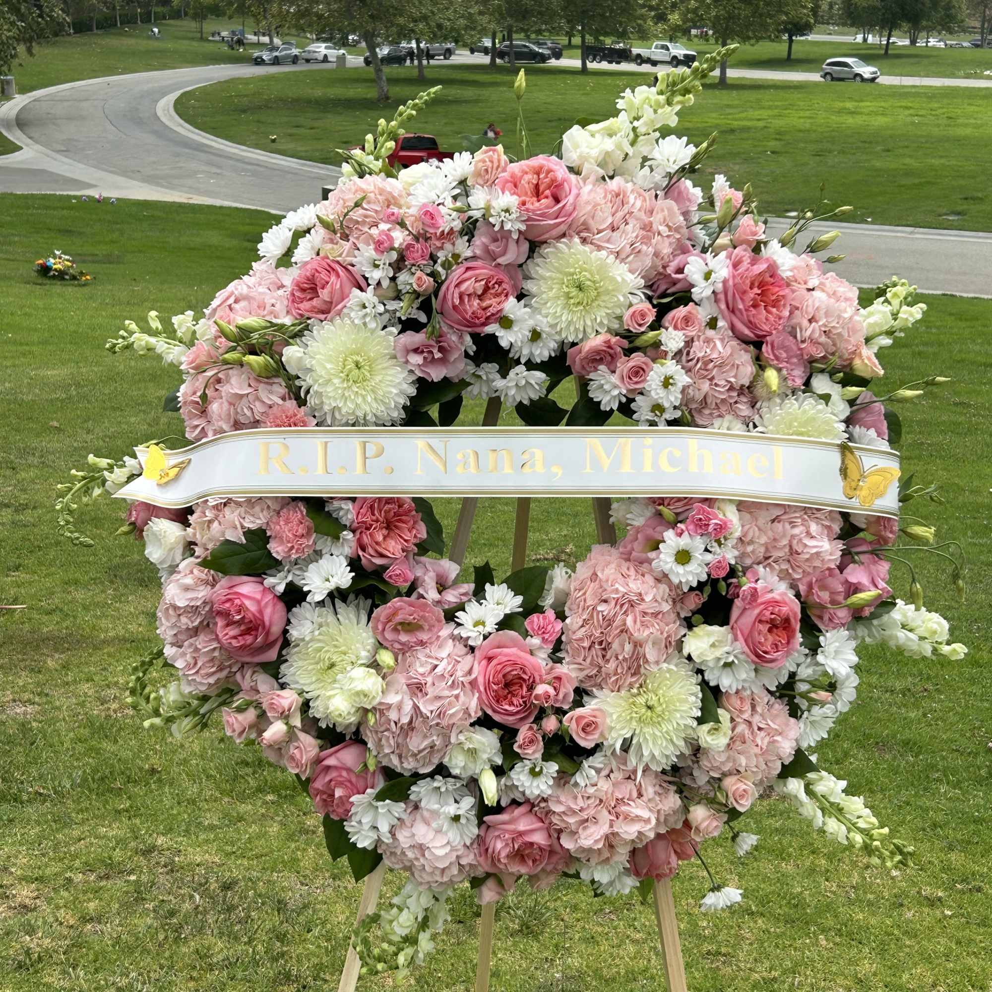 Pink and white funeral wreath on an easel with a memorial ribbon