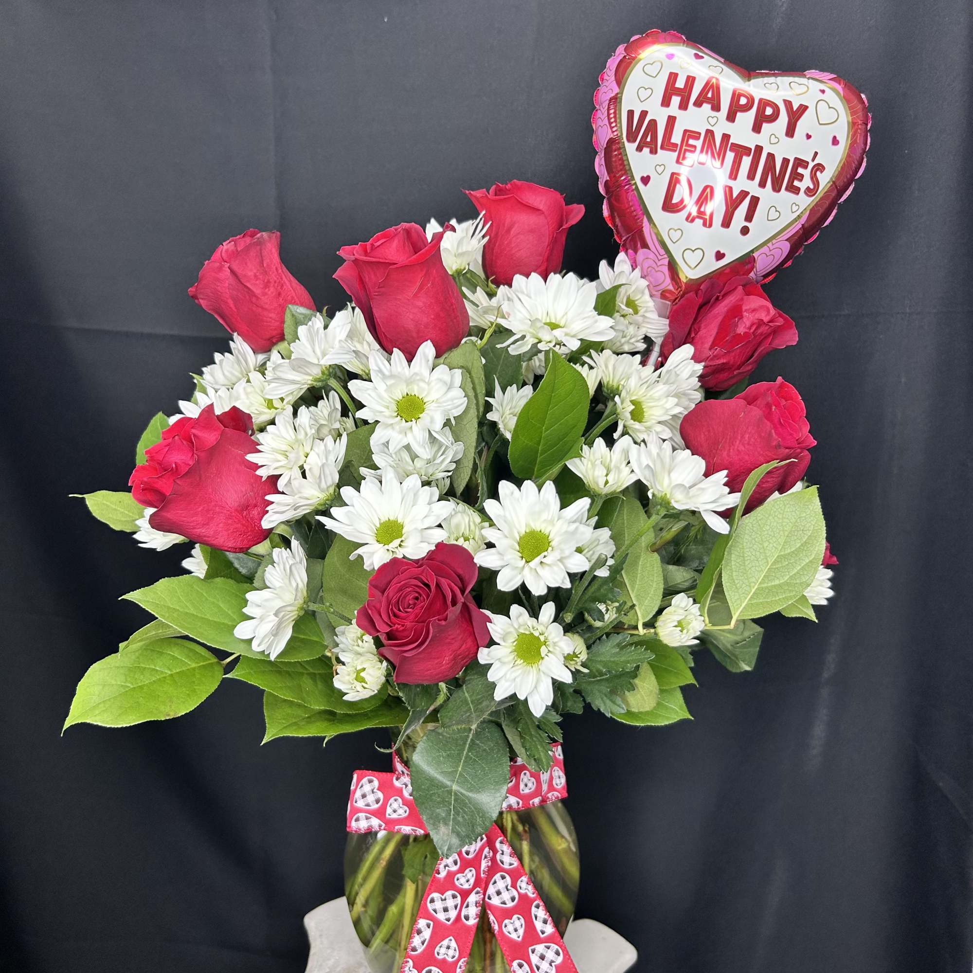 Bouquet of red roses and white daisies in a glass vase with a heart balloon