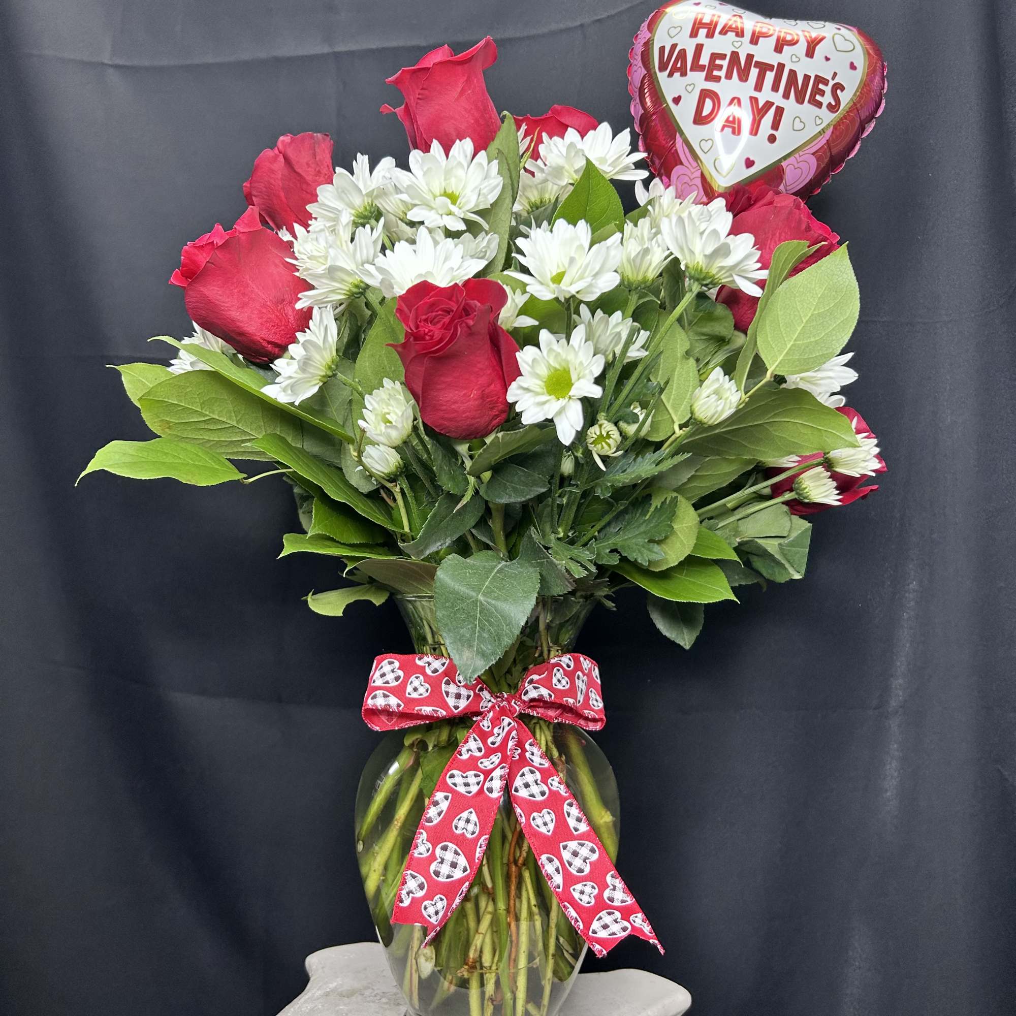 Red roses and white daisies in a glass vase with a Valentine balloon