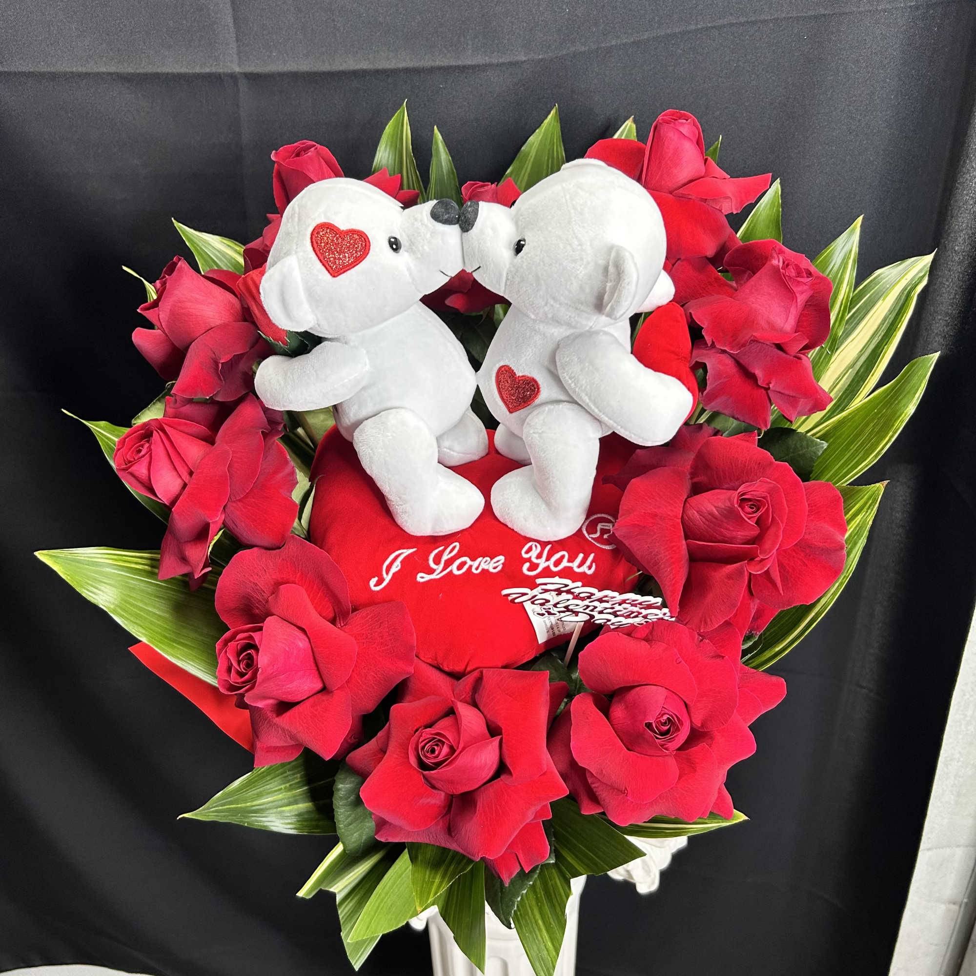 Red rose arrangement with two white teddy bears and a heart pillow