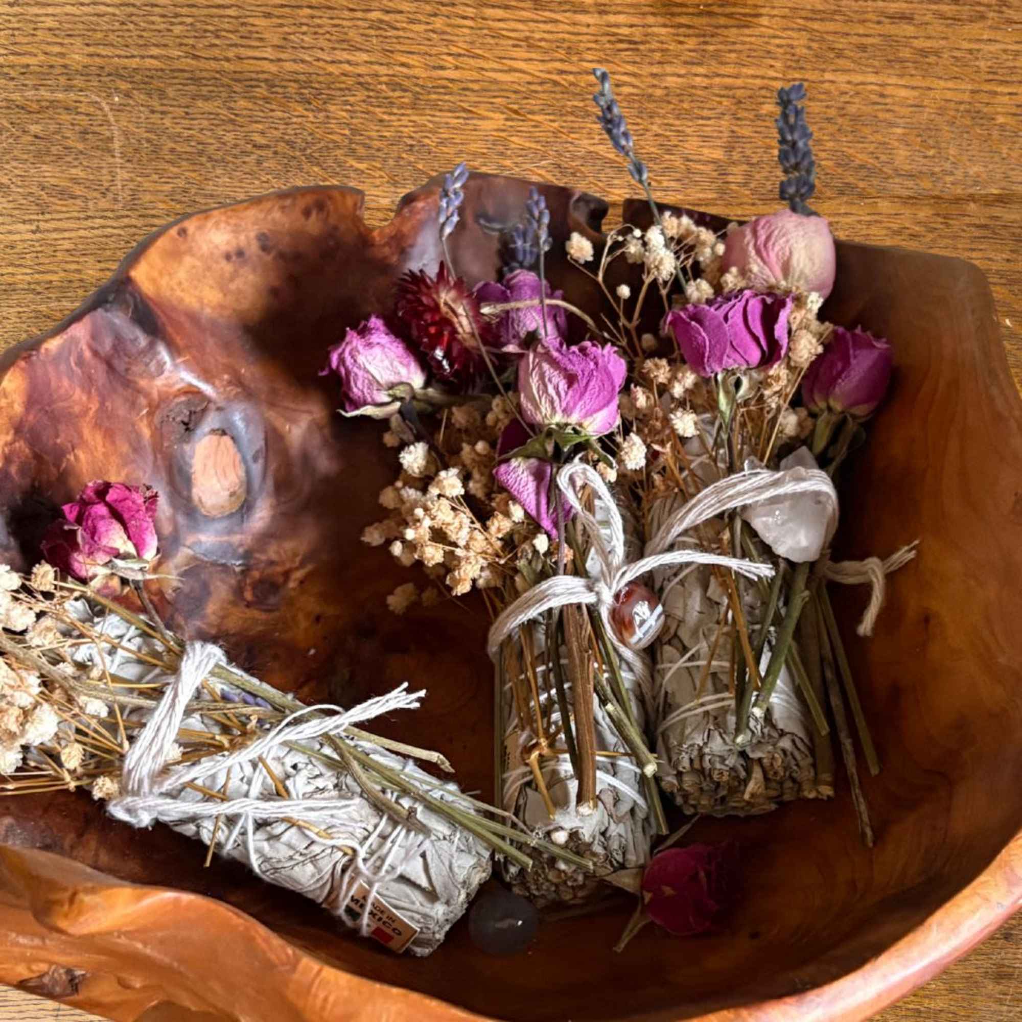 Bundles of dried pink roses and herbs tied with twine in a carved wooden bowl