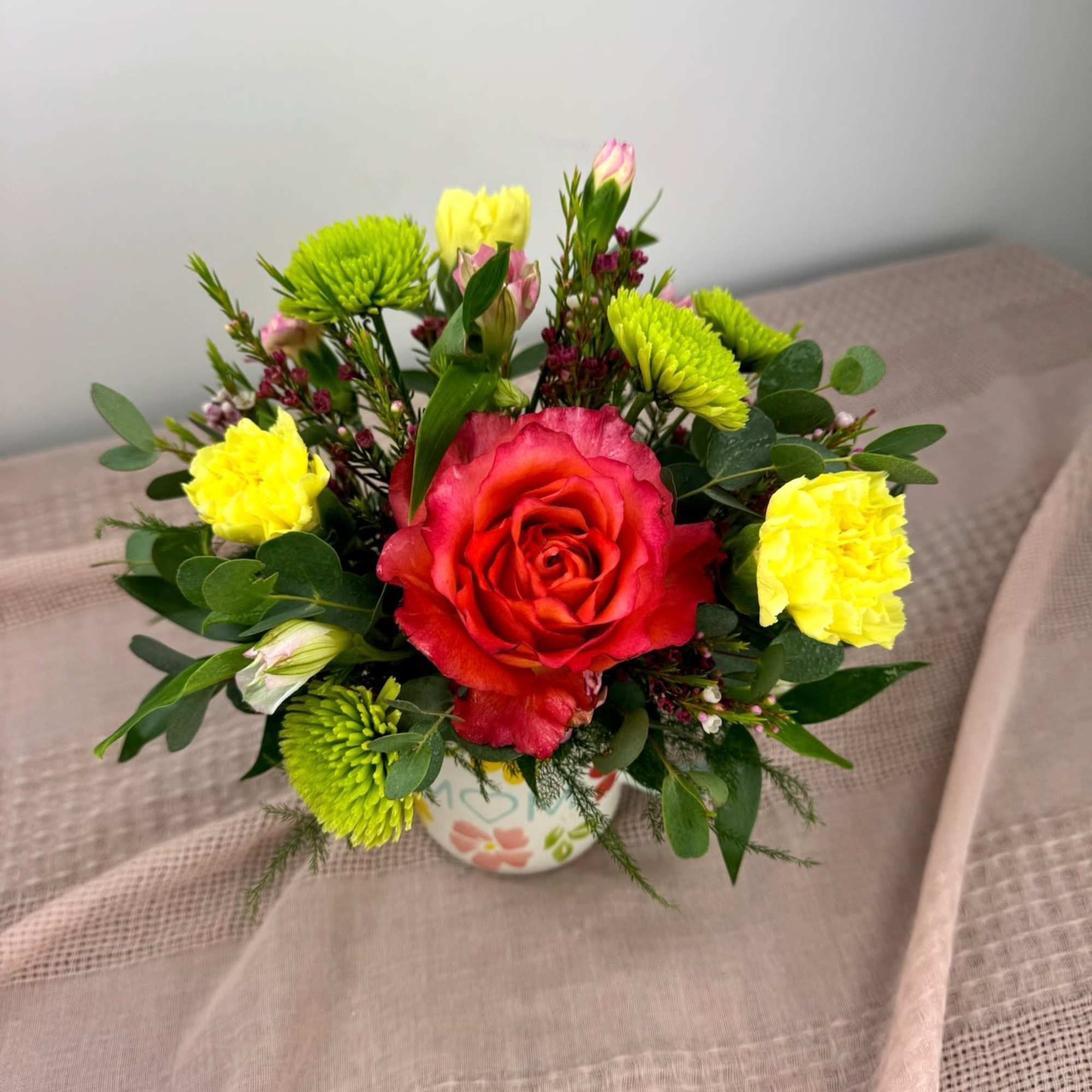 A cheerful bouquet arranged in a white ceramic mug printed with "MOM"
