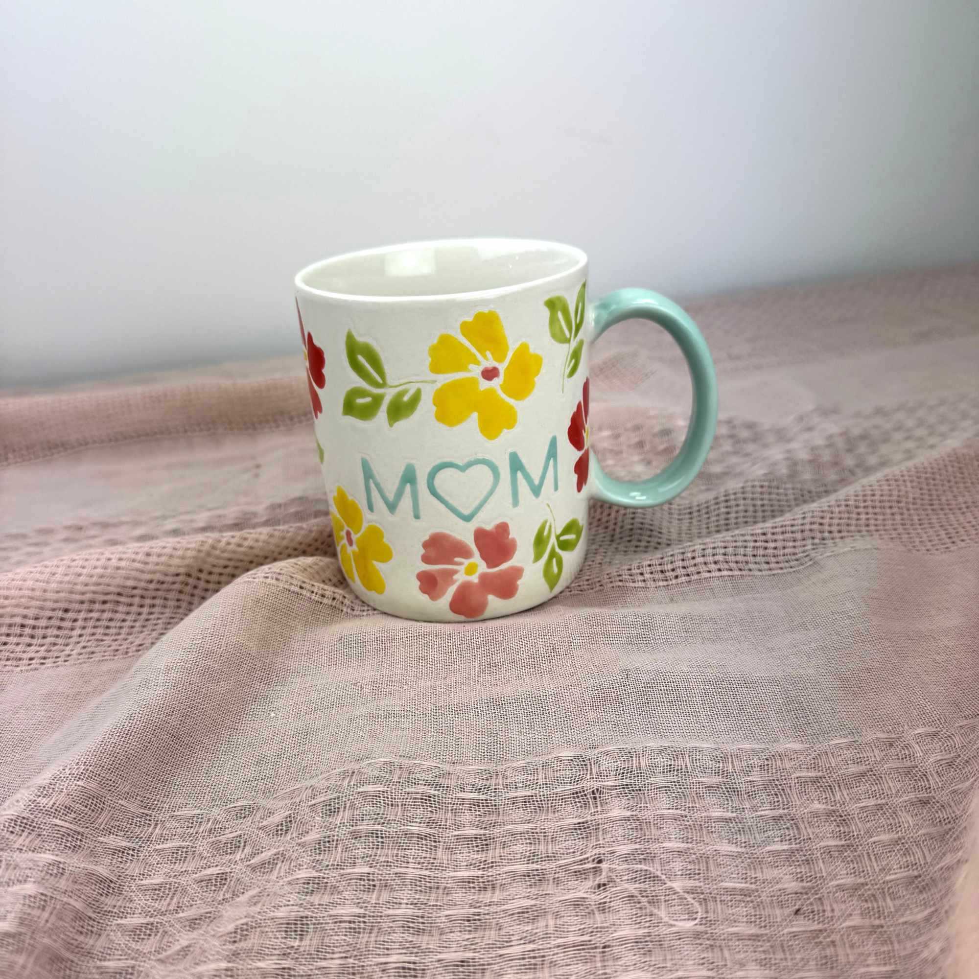 A cheerful bouquet arranged in a white ceramic mug printed with "MOM"