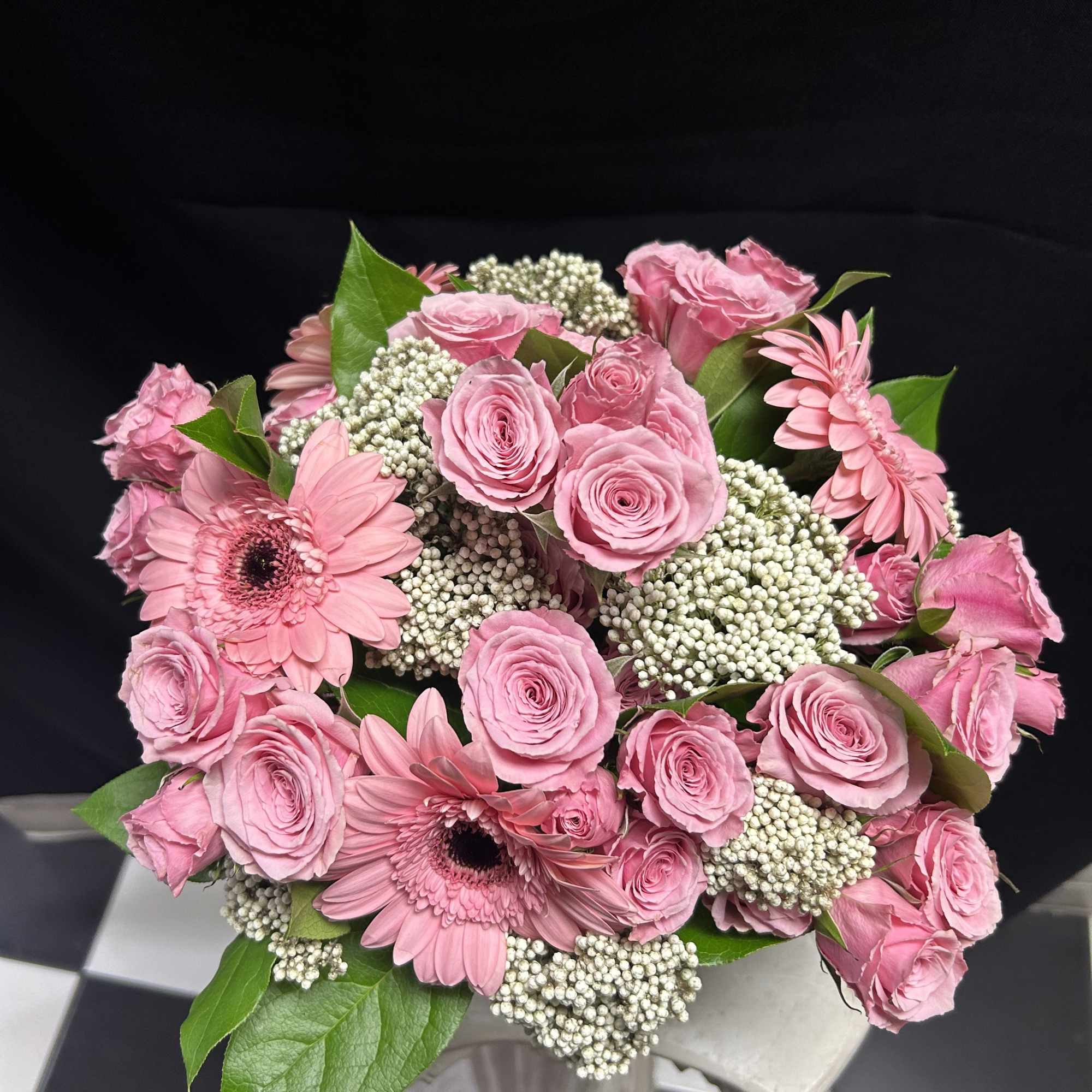 Pink roses and gerbera daisies arranged in a bouquet with white filler flowers.