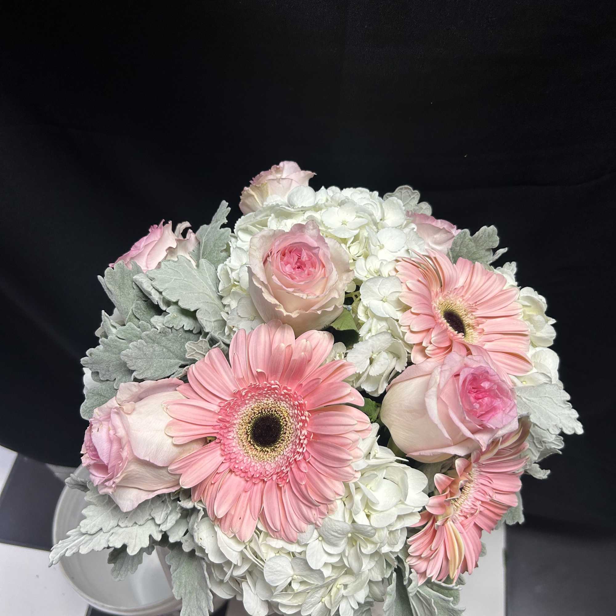 Pink gerbera daisies and roses arranged with white hydrangeas in a vase.