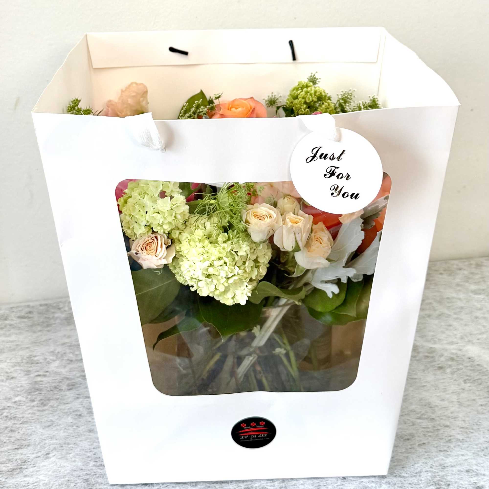Bouquet of pale roses and green hydrangeas in a white gift bag