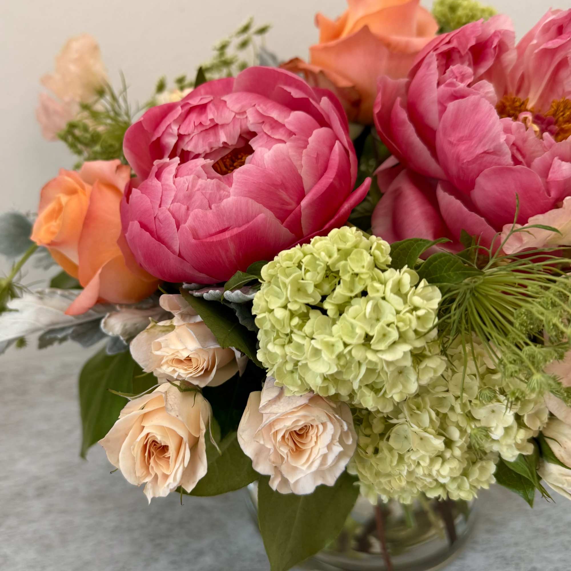 Bouquet of pink peonies, peach roses, and pale green hydrangeas in a glass vase