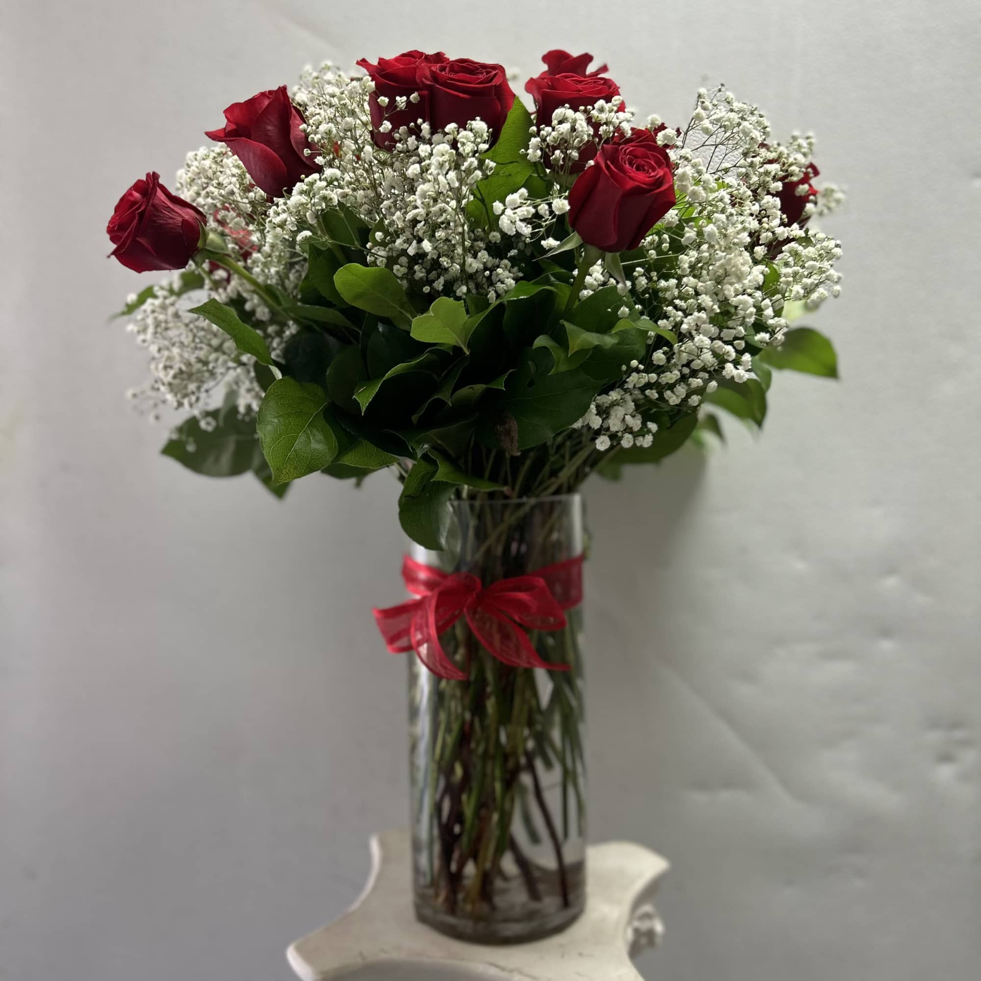 Red roses and baby's breath in a clear glass vase with a red ribbon