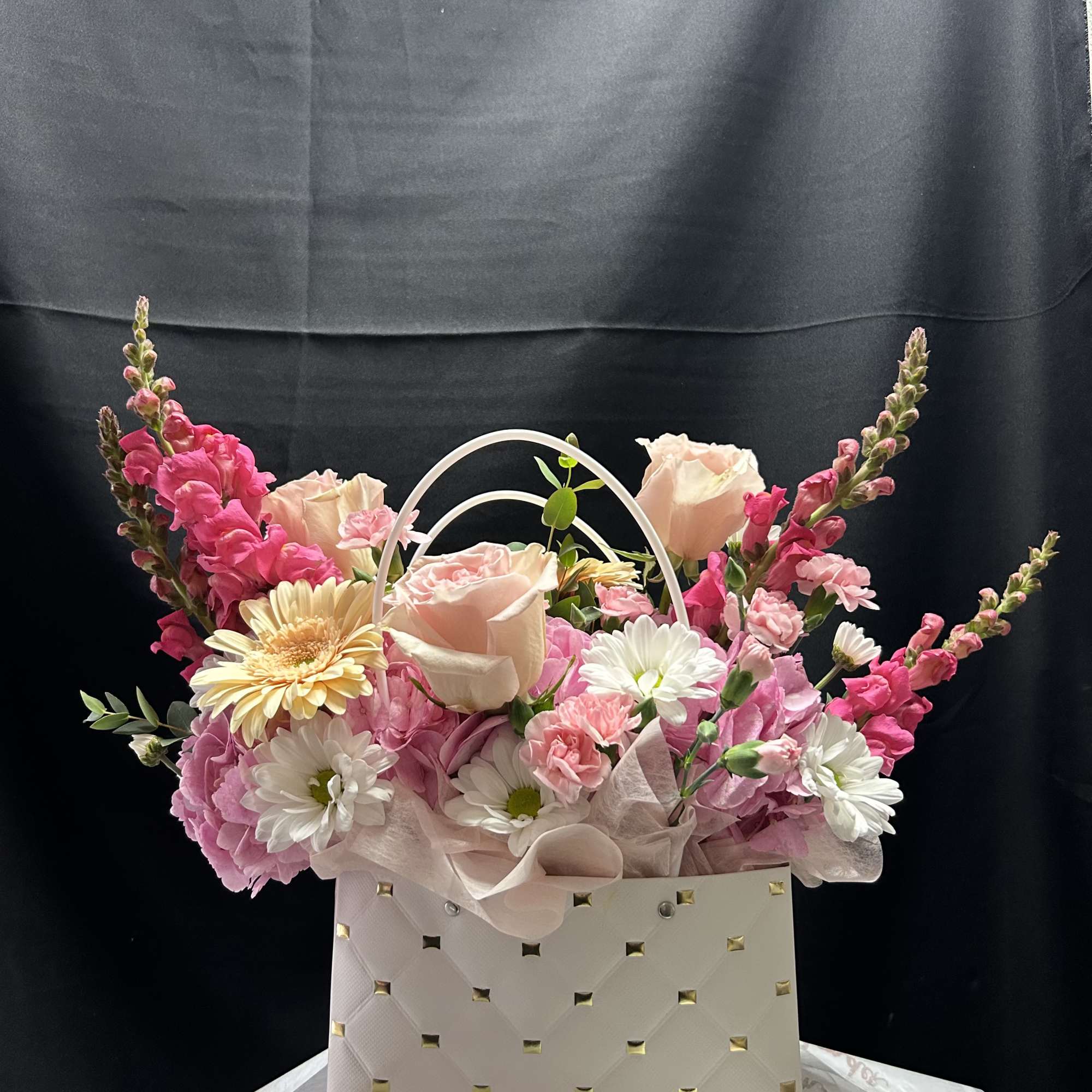 An assortment of small, dainty flowers styled to fit a bag-shaped vase.