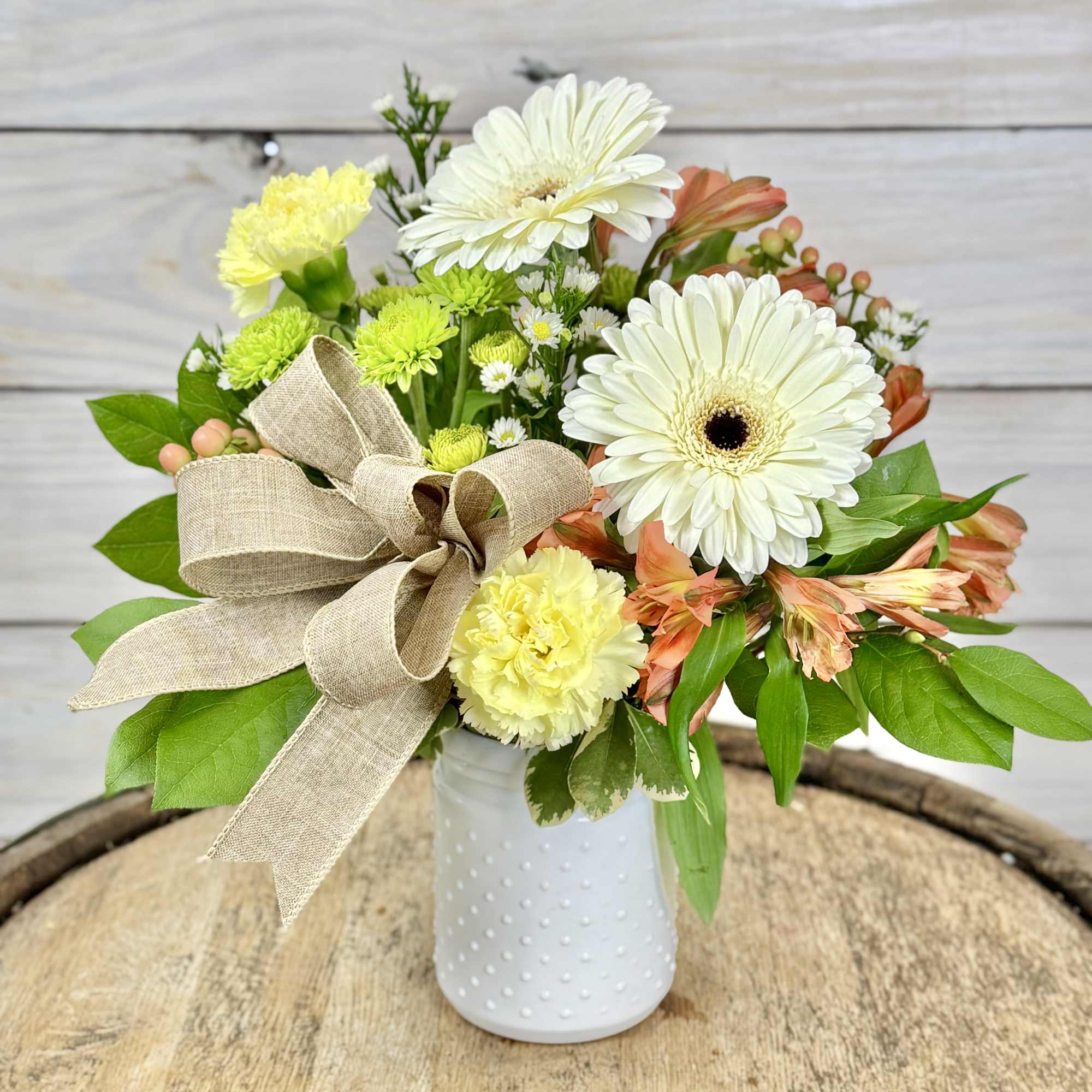 Mixed bouquet of white daisies and yellow carnations in a white vase with a burlap bow