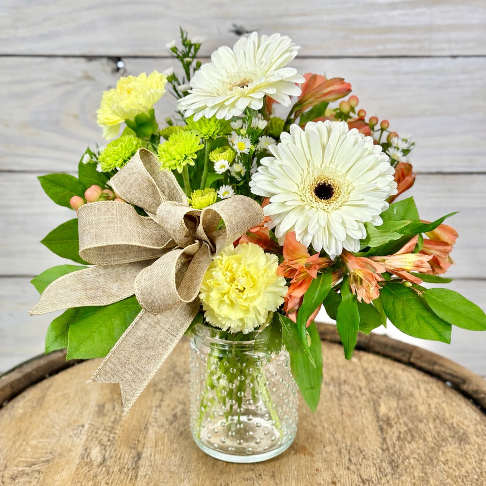 A cute and rustic flower arrangement nestled in a clear hobnail jar.