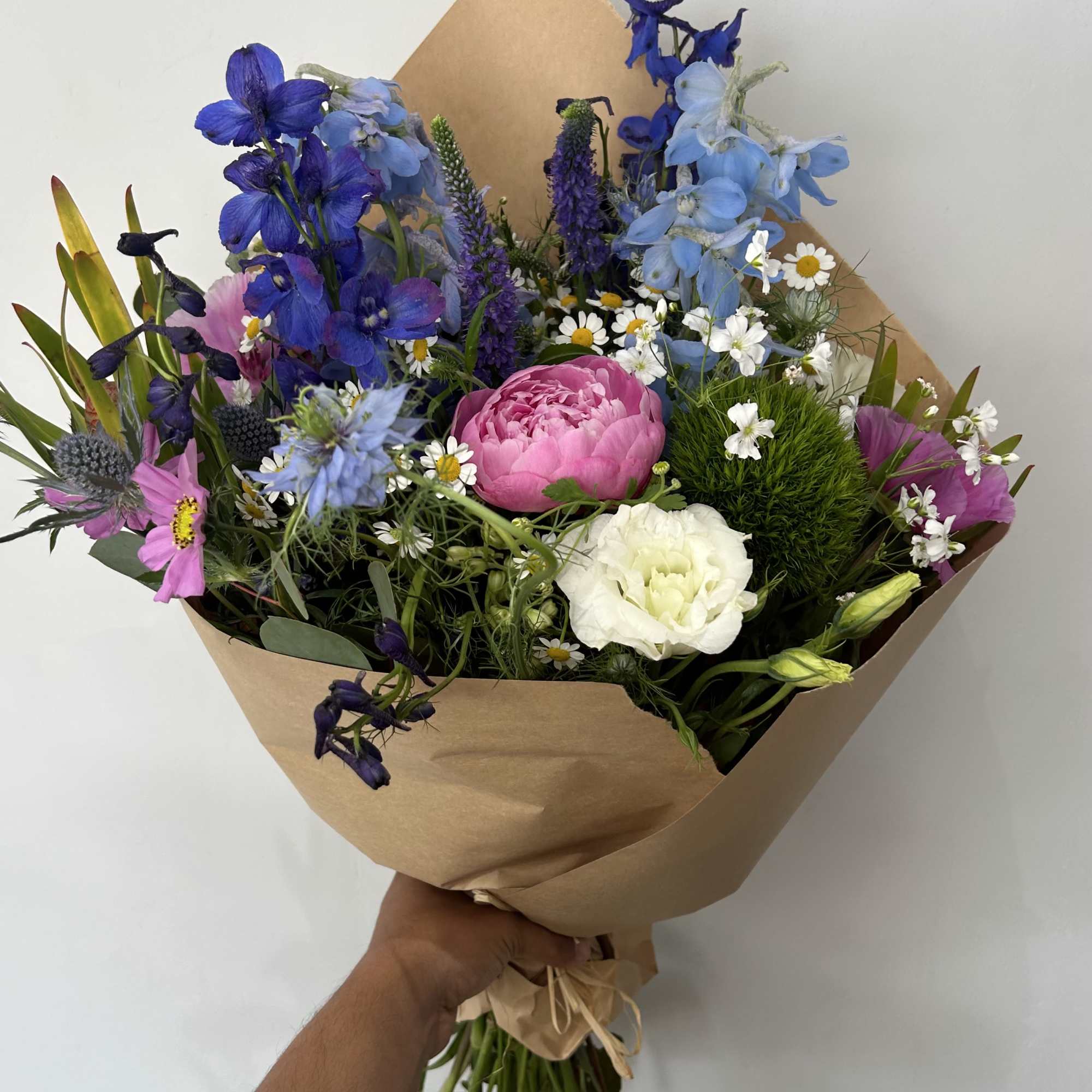 Hand-tied bouquet of blue, pink, and white flowers wrapped in brown paper