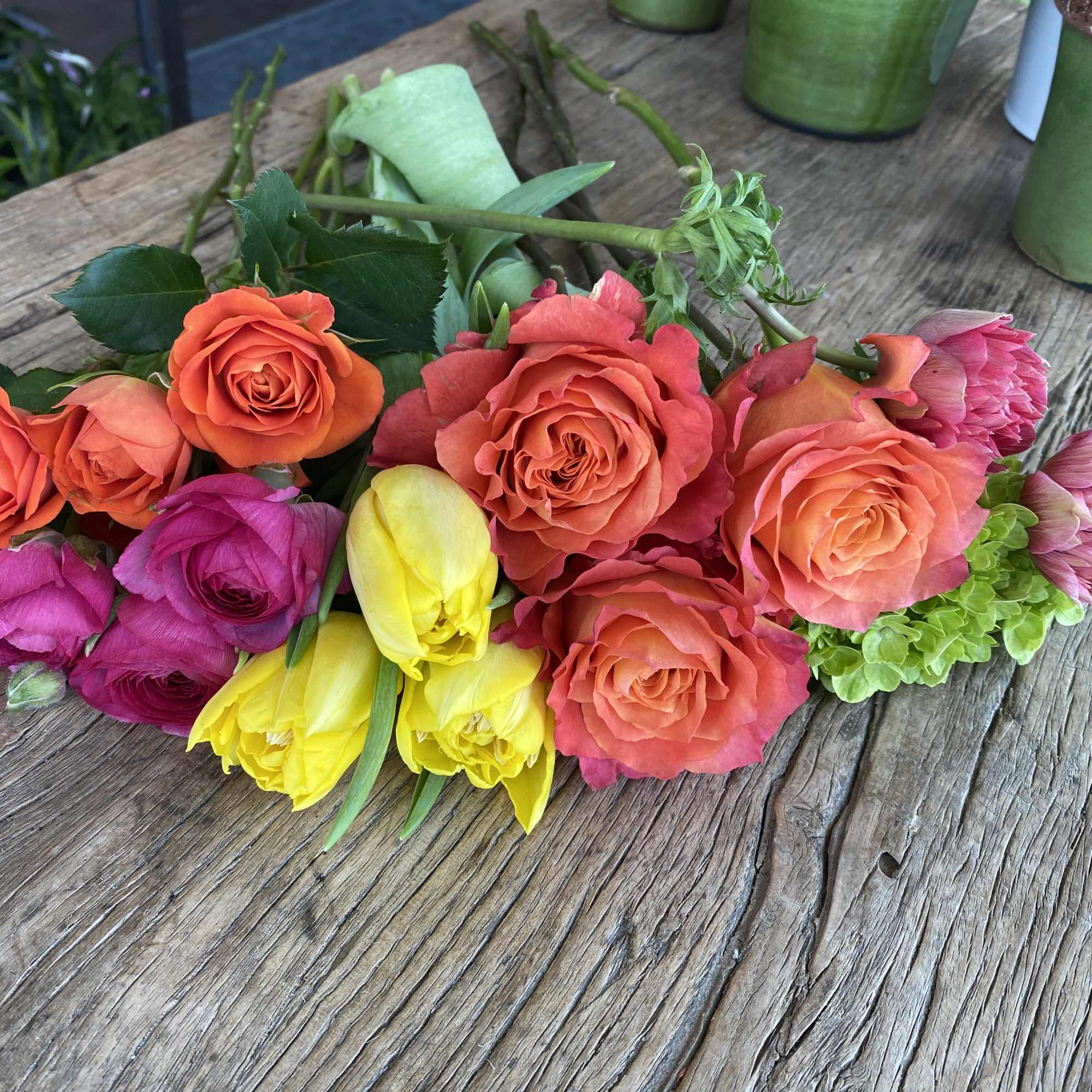 Mixed bouquet of orange, pink, and yellow roses with green accents