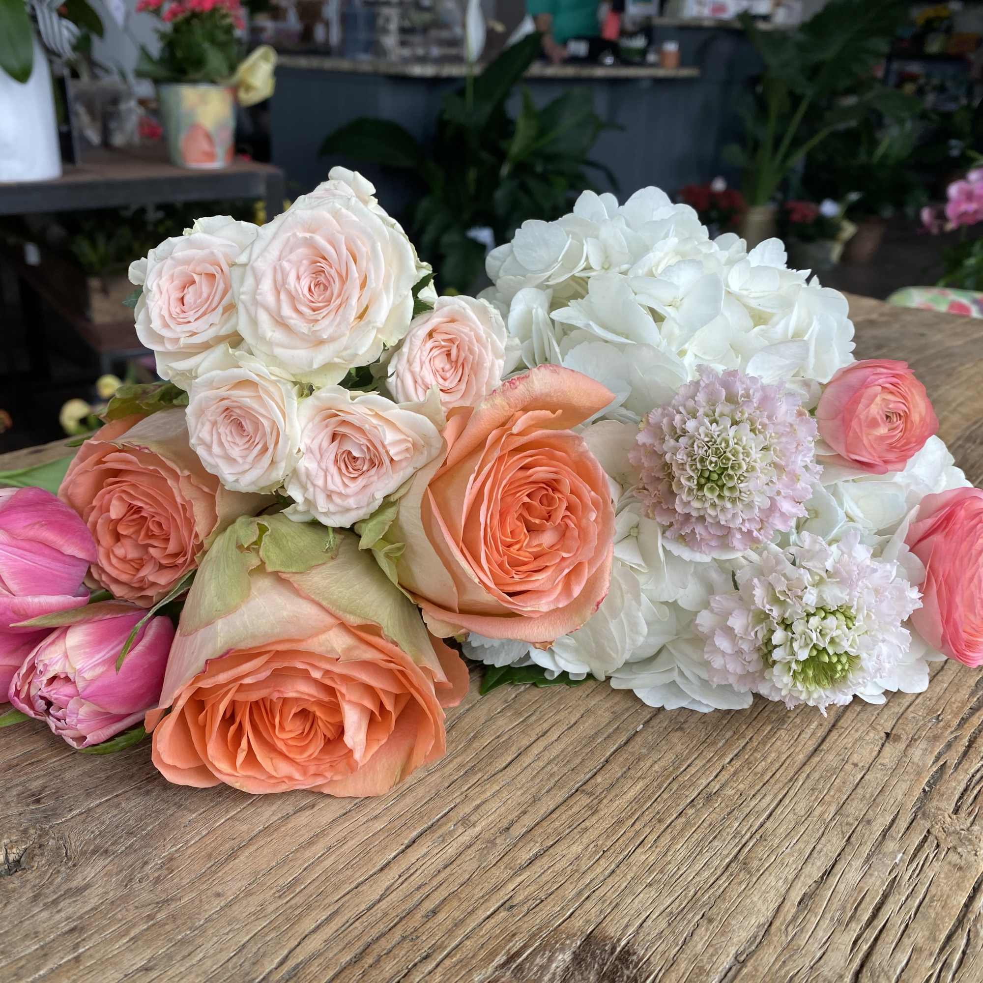 Assorted pink, peach, and white flowers arranged on a wooden table