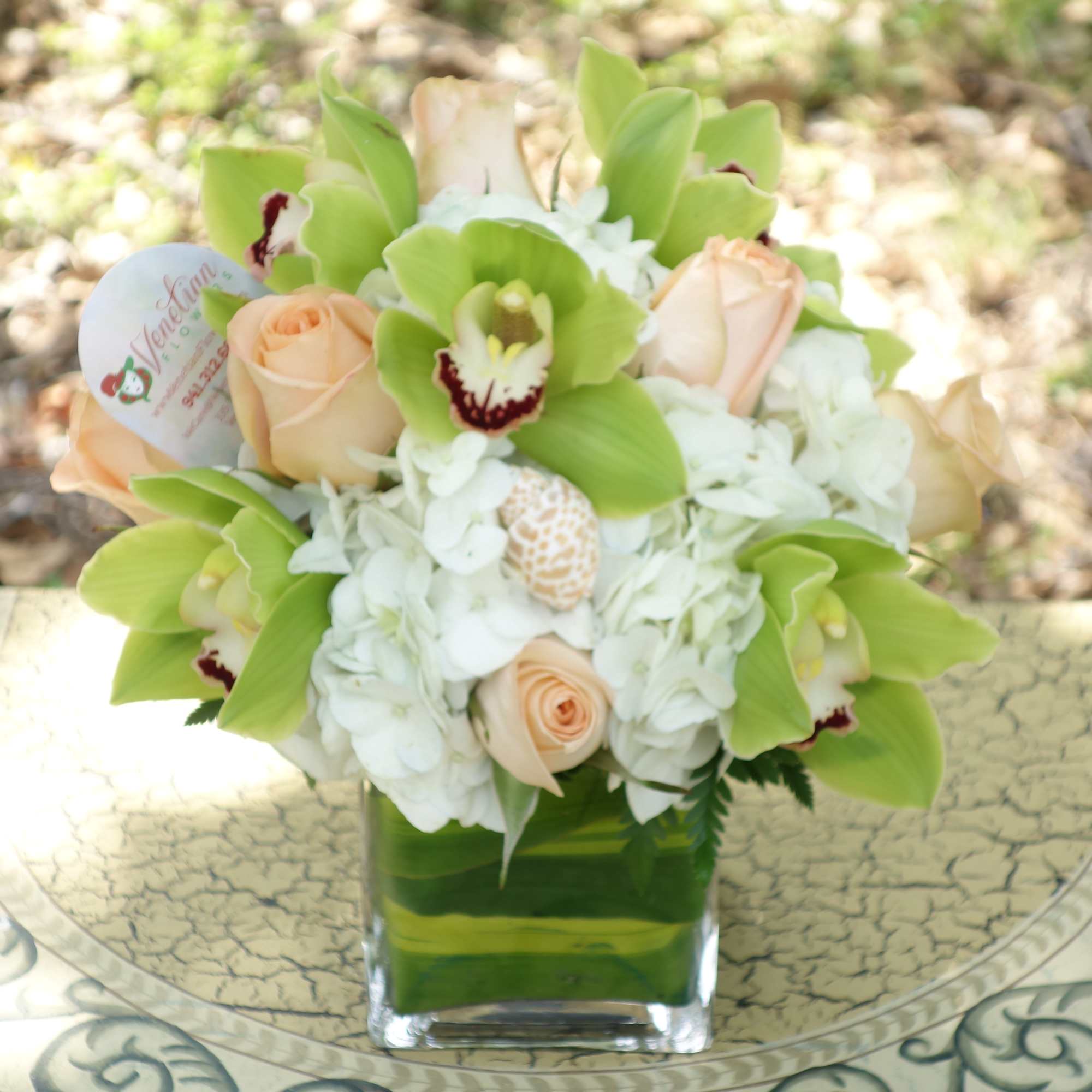 Peach roses and green orchids in a square glass vase