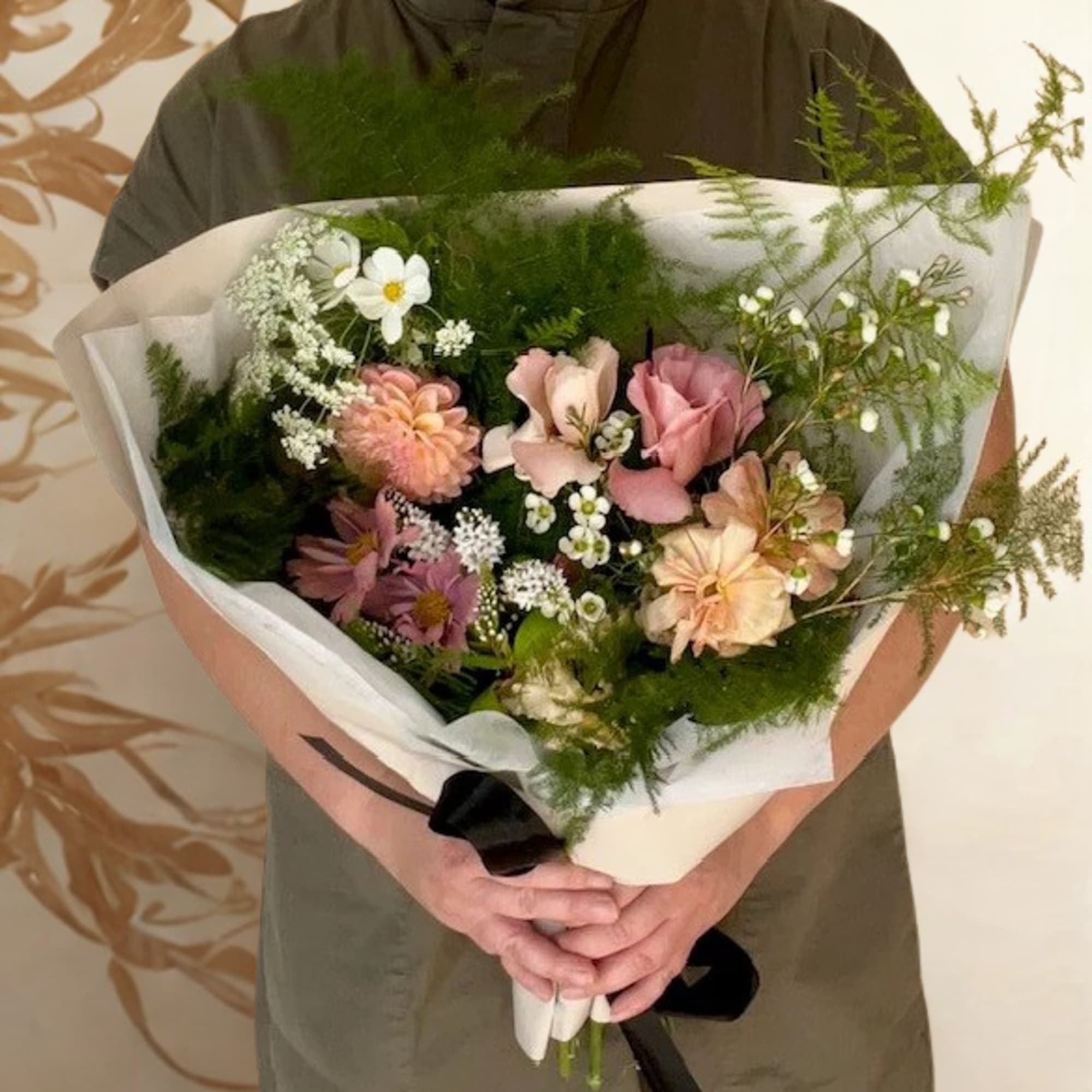 Handheld bouquet of pink and white flowers wrapped in paper