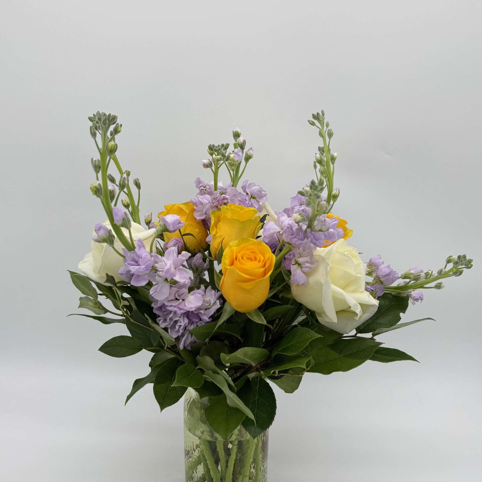 Bouquet of yellow and white roses with lavender flowers in a glass vase