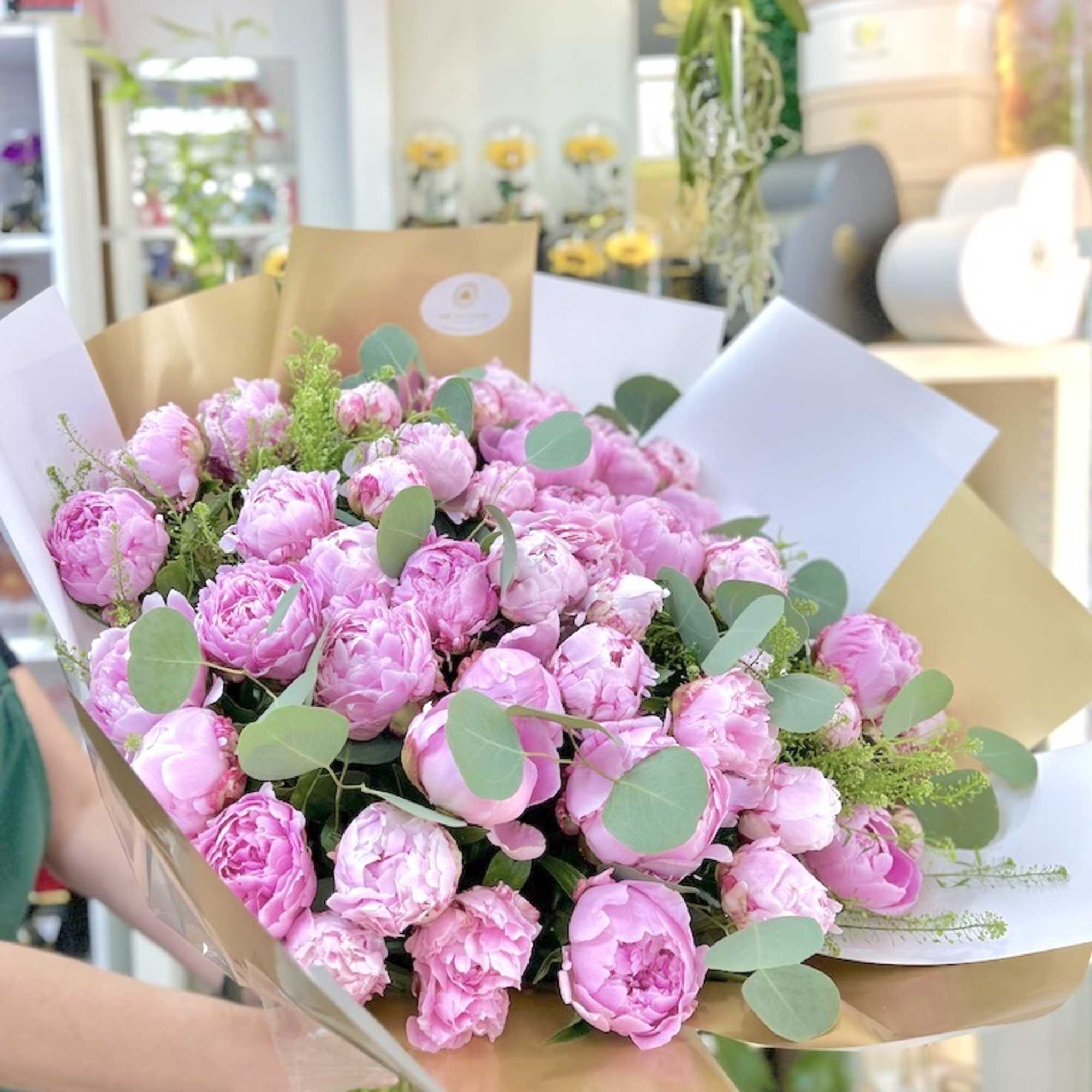 Large hand-tied bouquet of pink peonies wrapped in white and gold paper