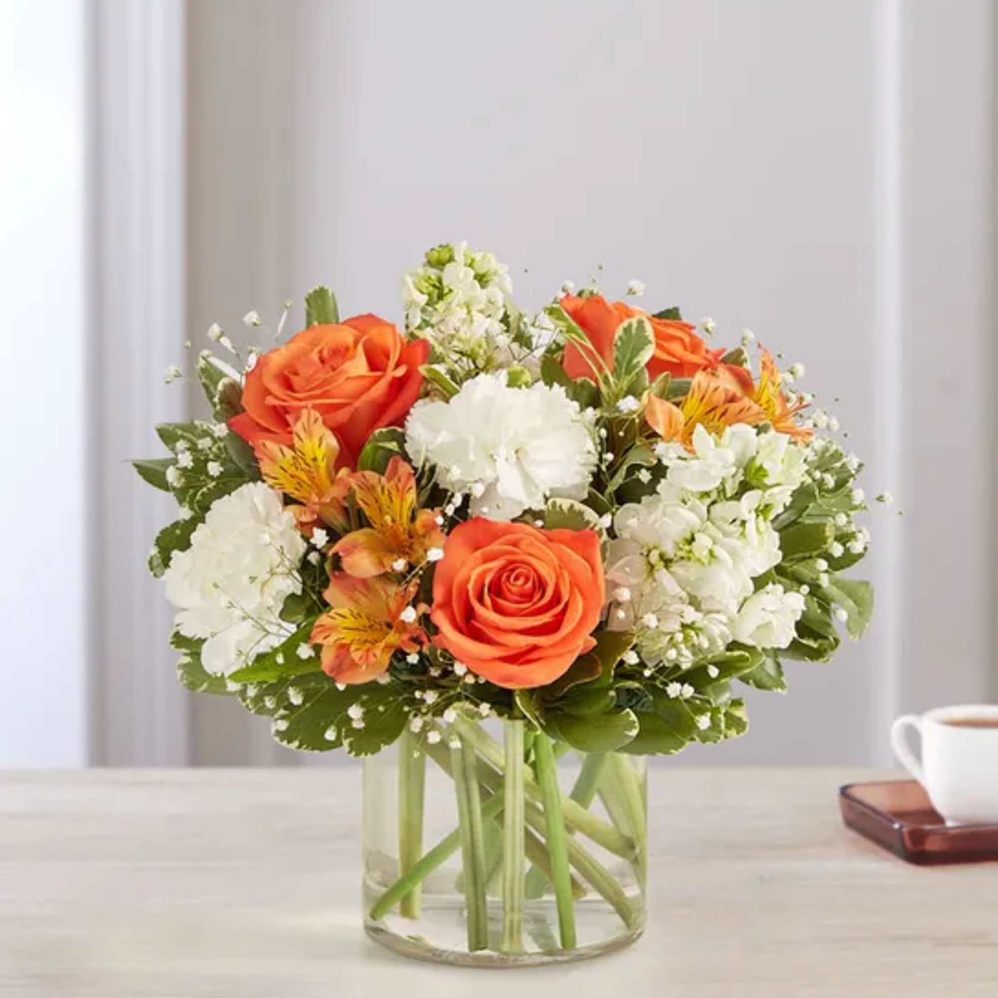 Orange roses and white flowers arranged in a clear glass vase