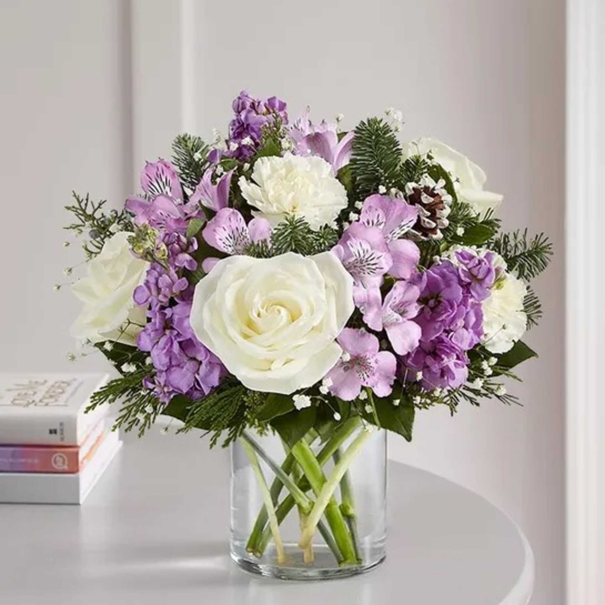 White roses and purple flowers arranged in a clear glass vase