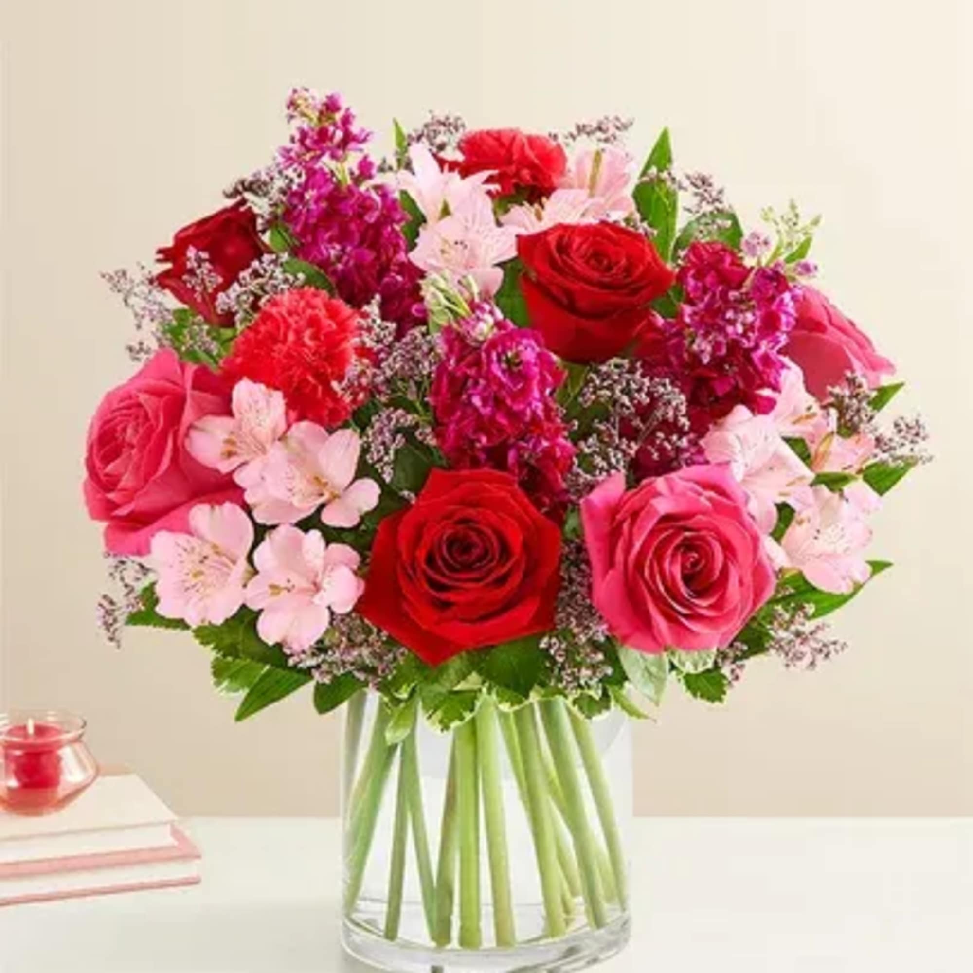 Bouquet of red and pink roses with pale pink filler flowers in a clear glass vase