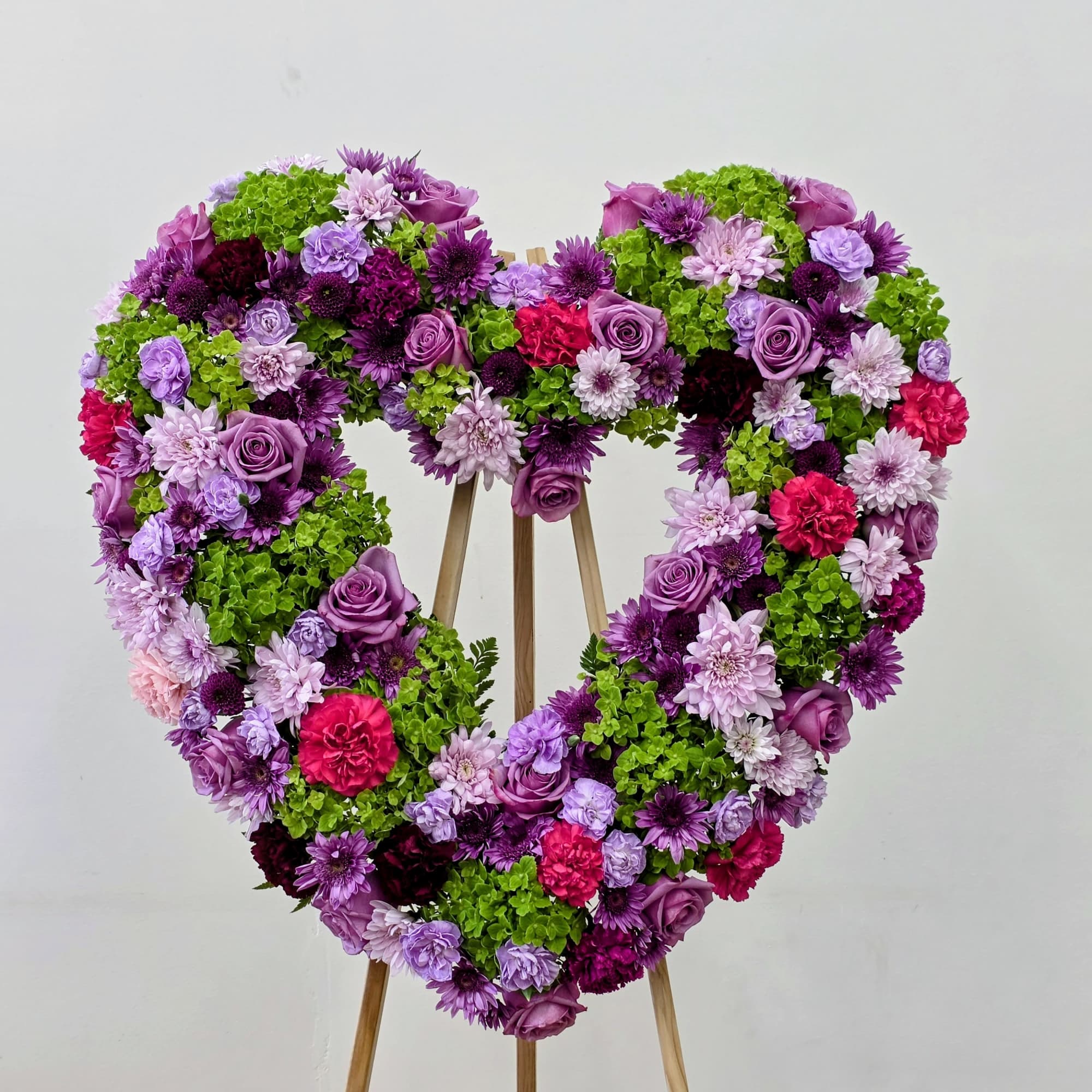 A large heart-shaped wreath bursting with purple roses, pink carnations, lavender and