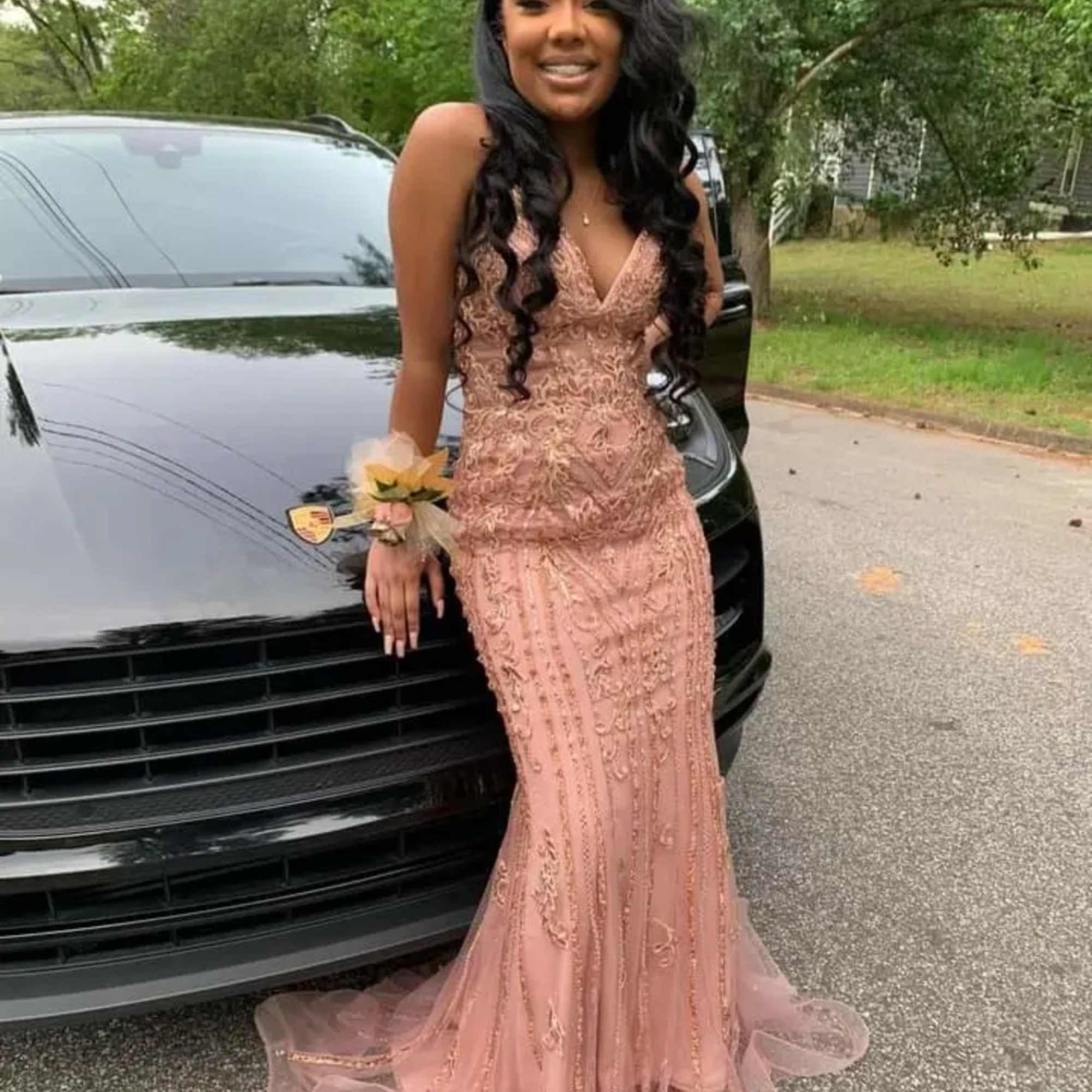 Woman in a blush gown with a floral wrist corsage standing by a black car