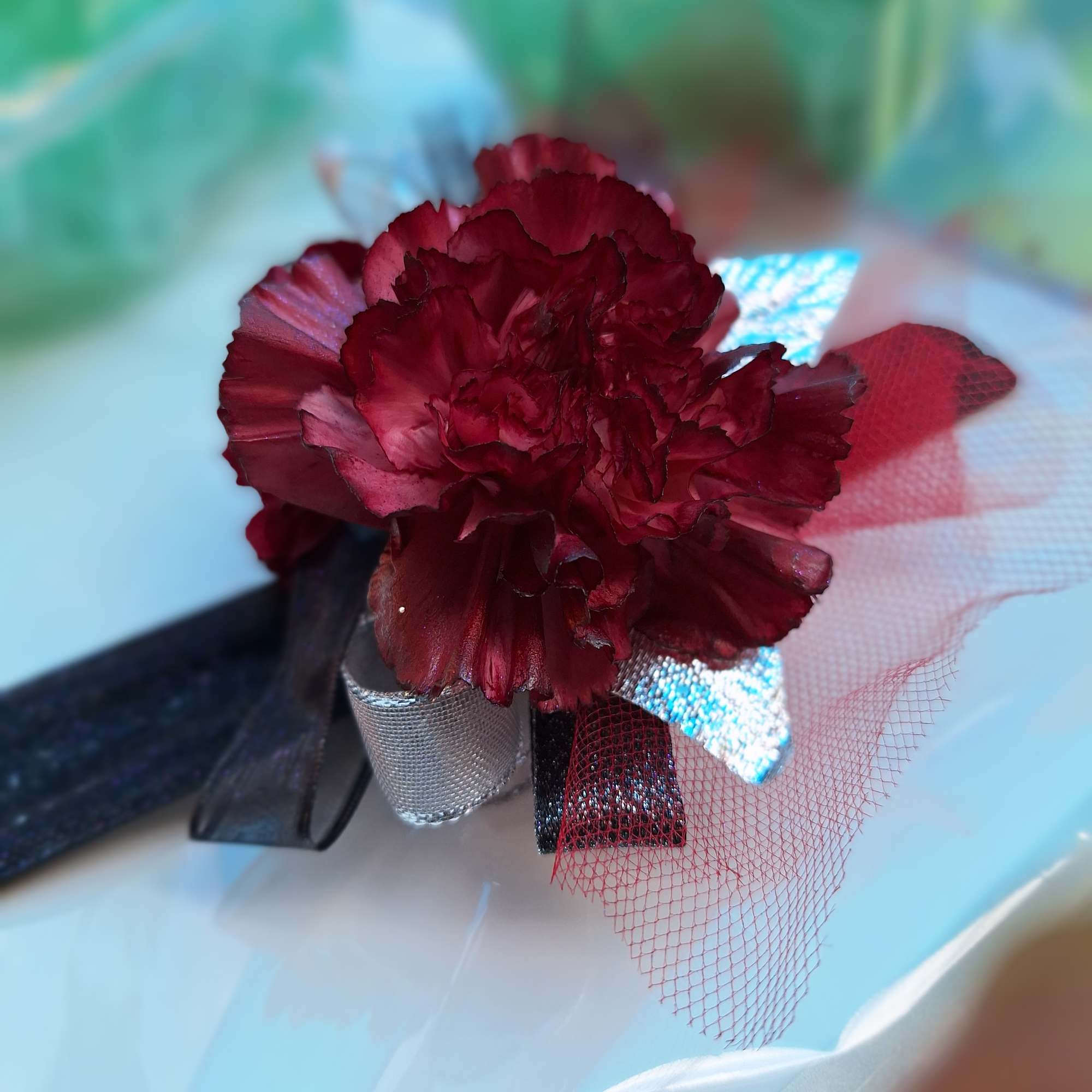 Single dark red carnation with decorative ribbon wrap