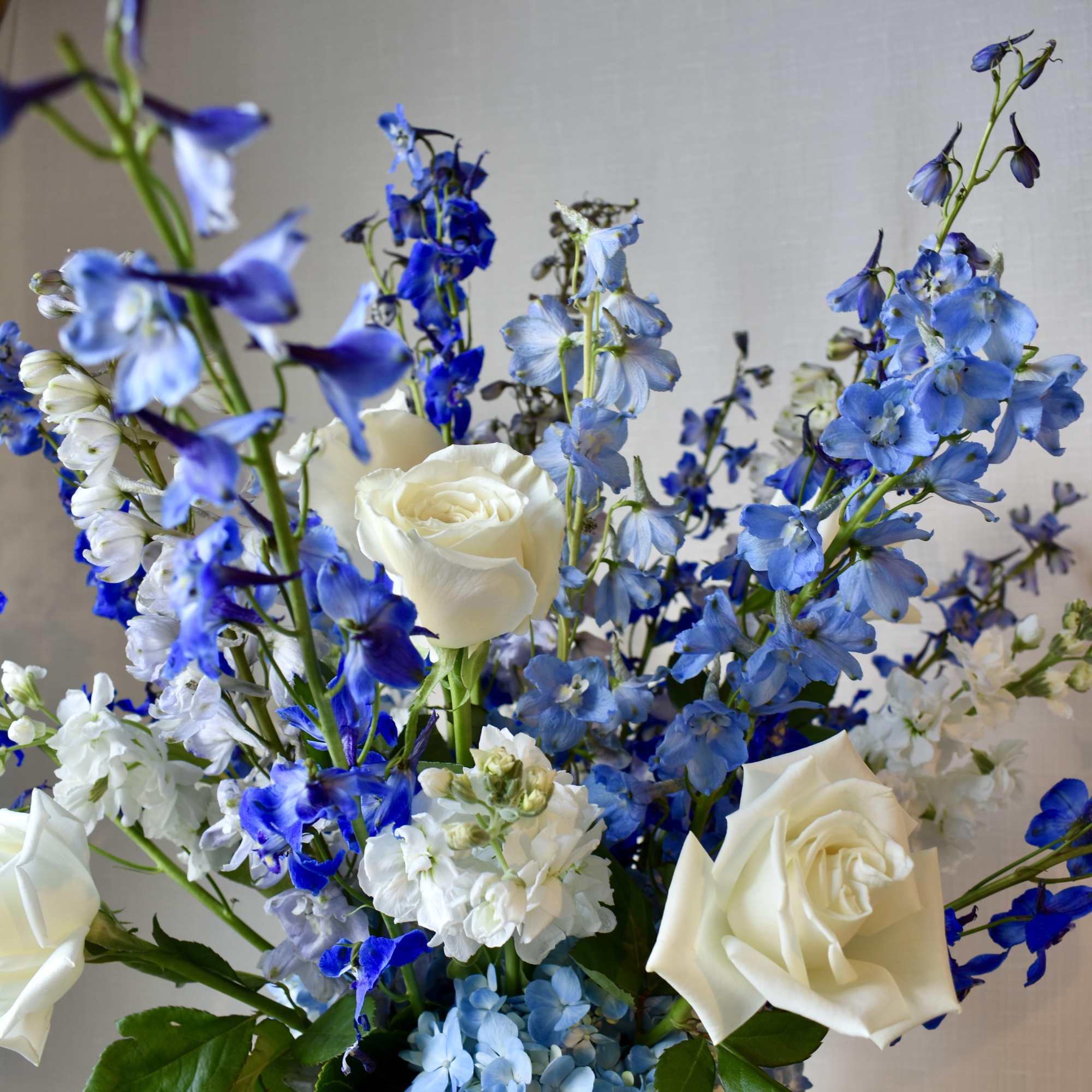 Tall arrangement of white roses with blue and white delphinium and blue hydrangea blooms.