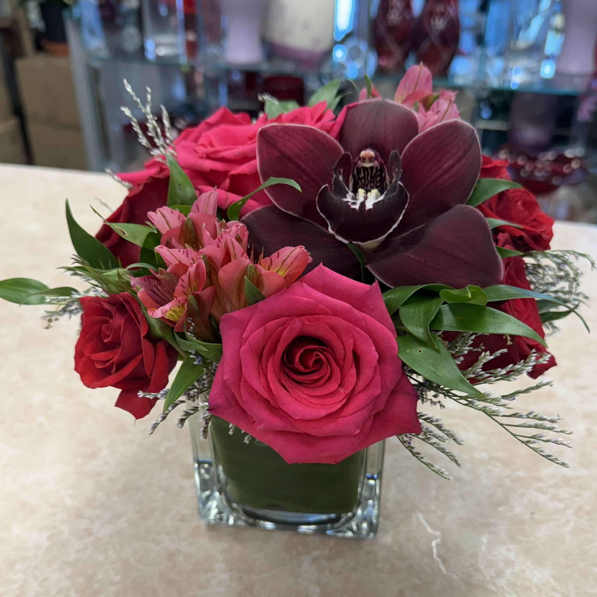 Pink and red roses with a dark orchid in a square glass vase