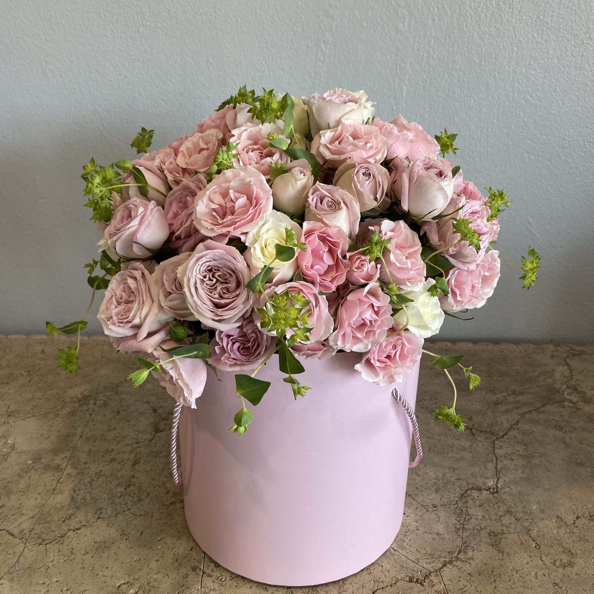 Pink roses and carnations arranged in a pastel pink hatbox