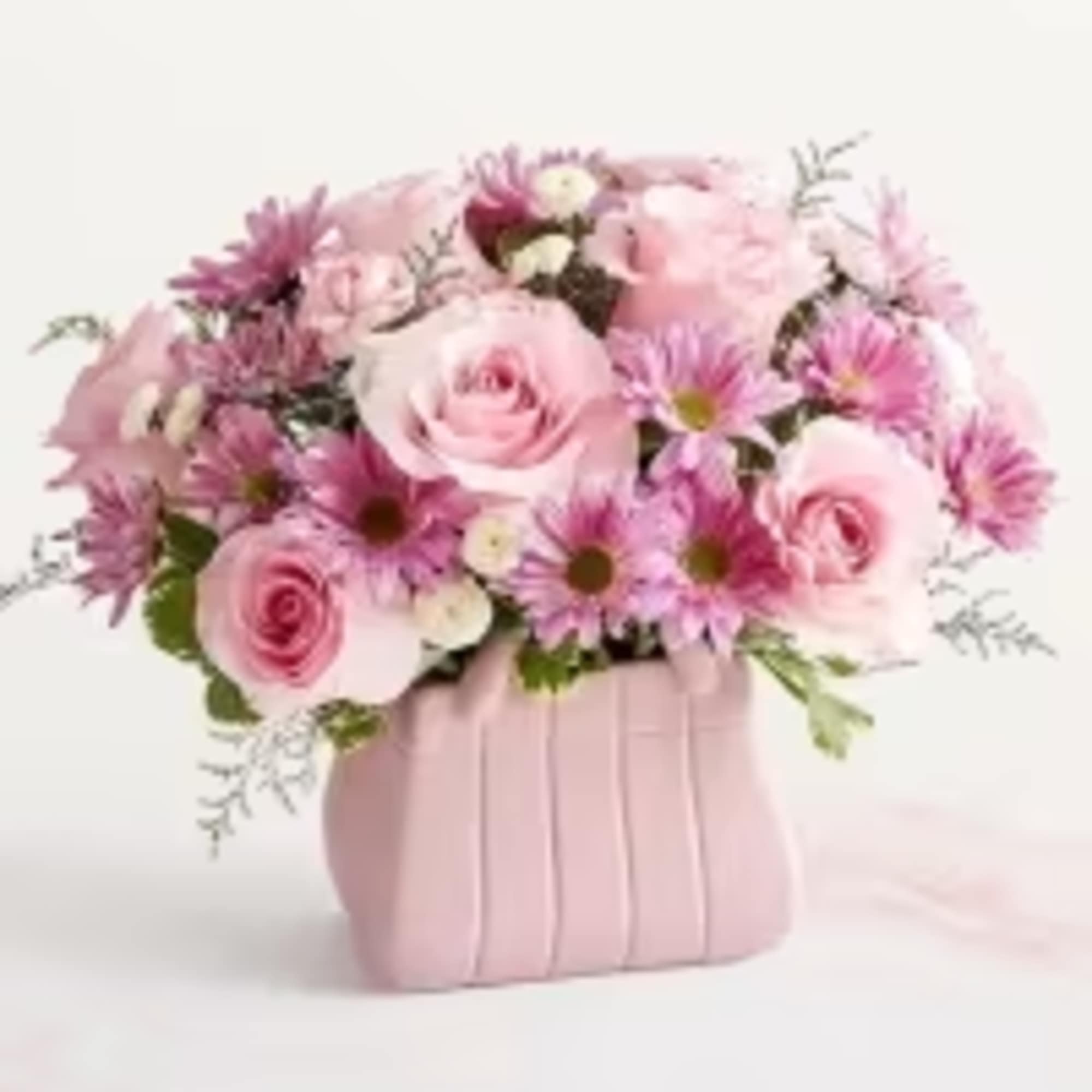 Pink roses and daisy-like blooms arranged in a pink purse-shaped ceramic vase