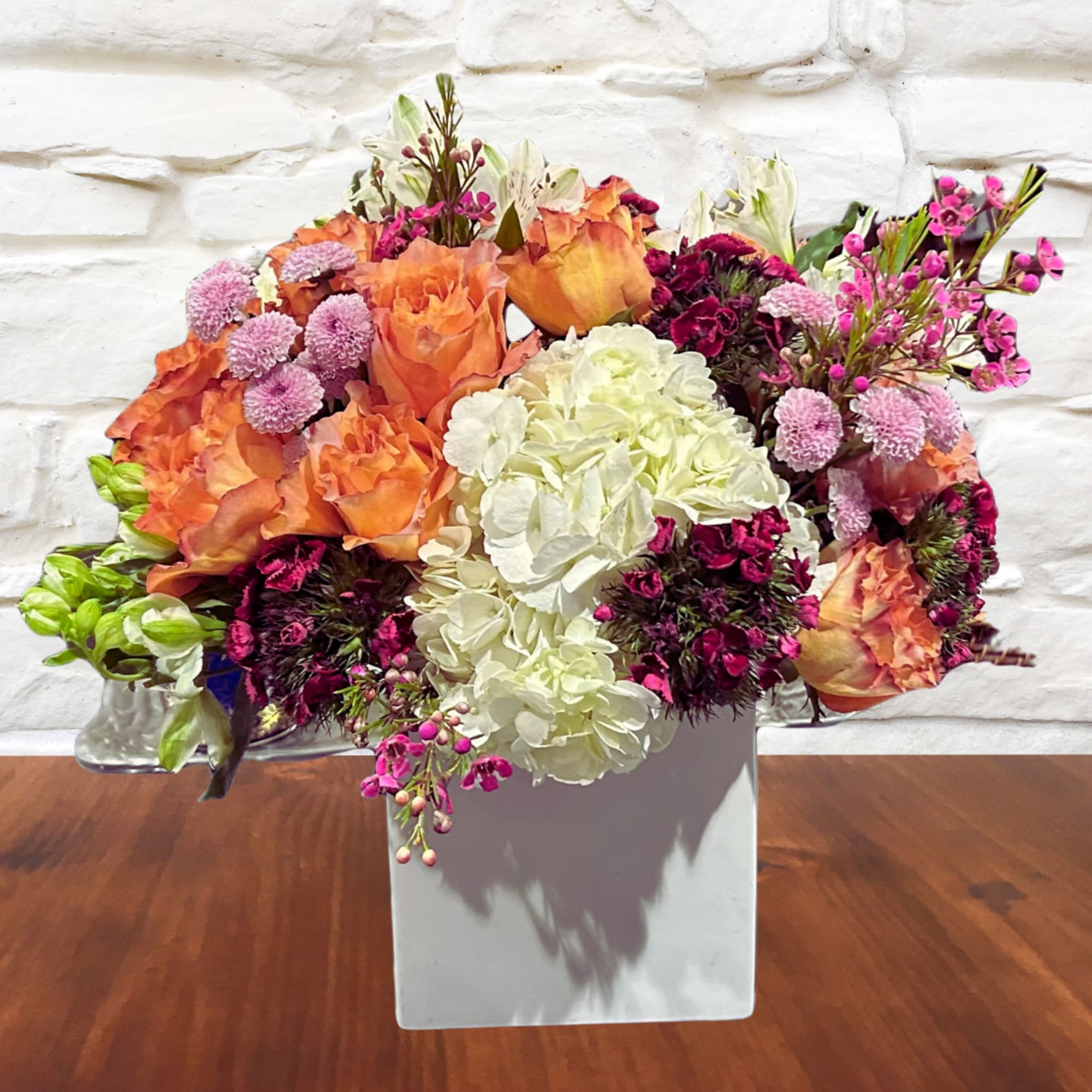 Mixed bouquet of orange, white, and magenta flowers in a white vase