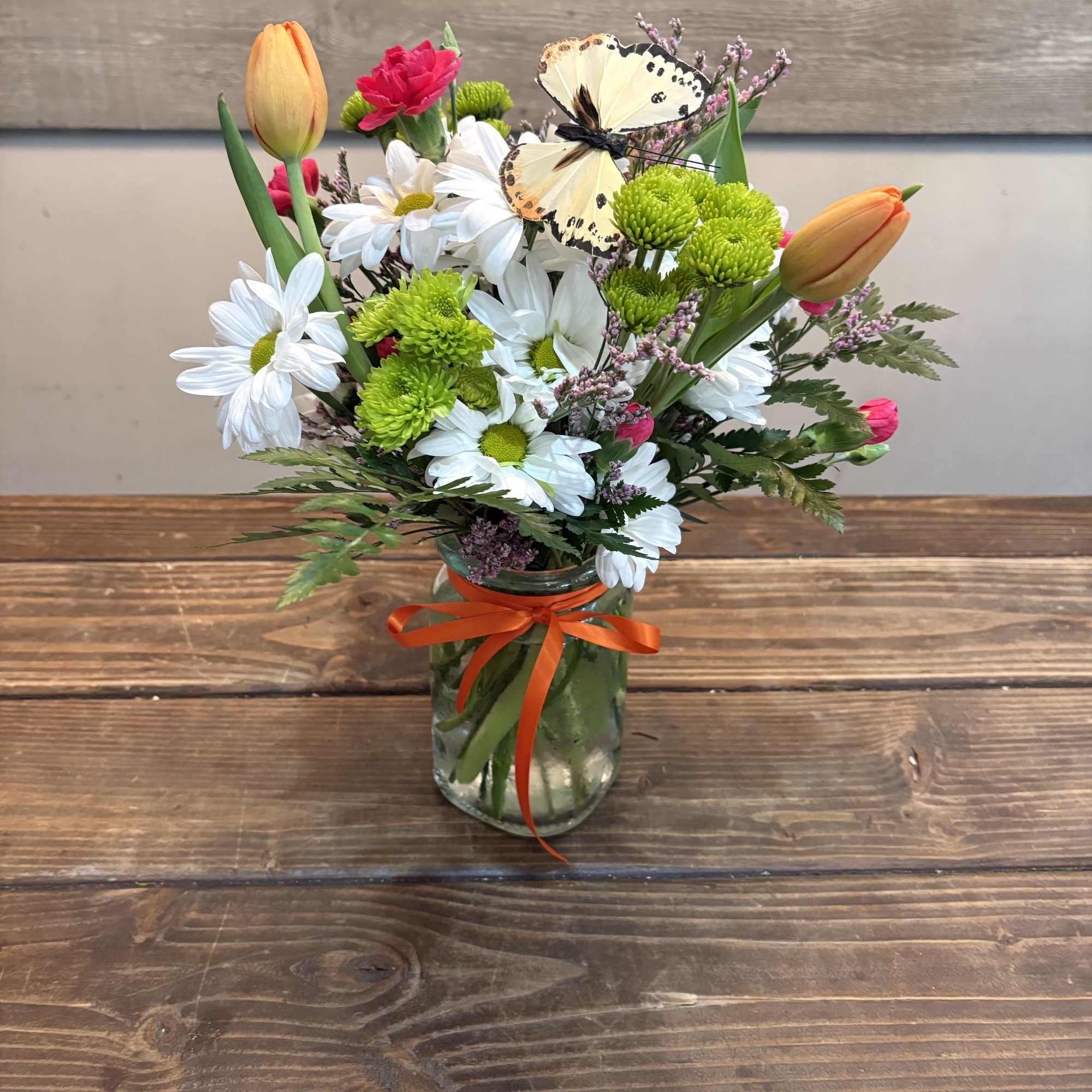 A cheerful cluster of orange tulips and crisp white daisies topped with
