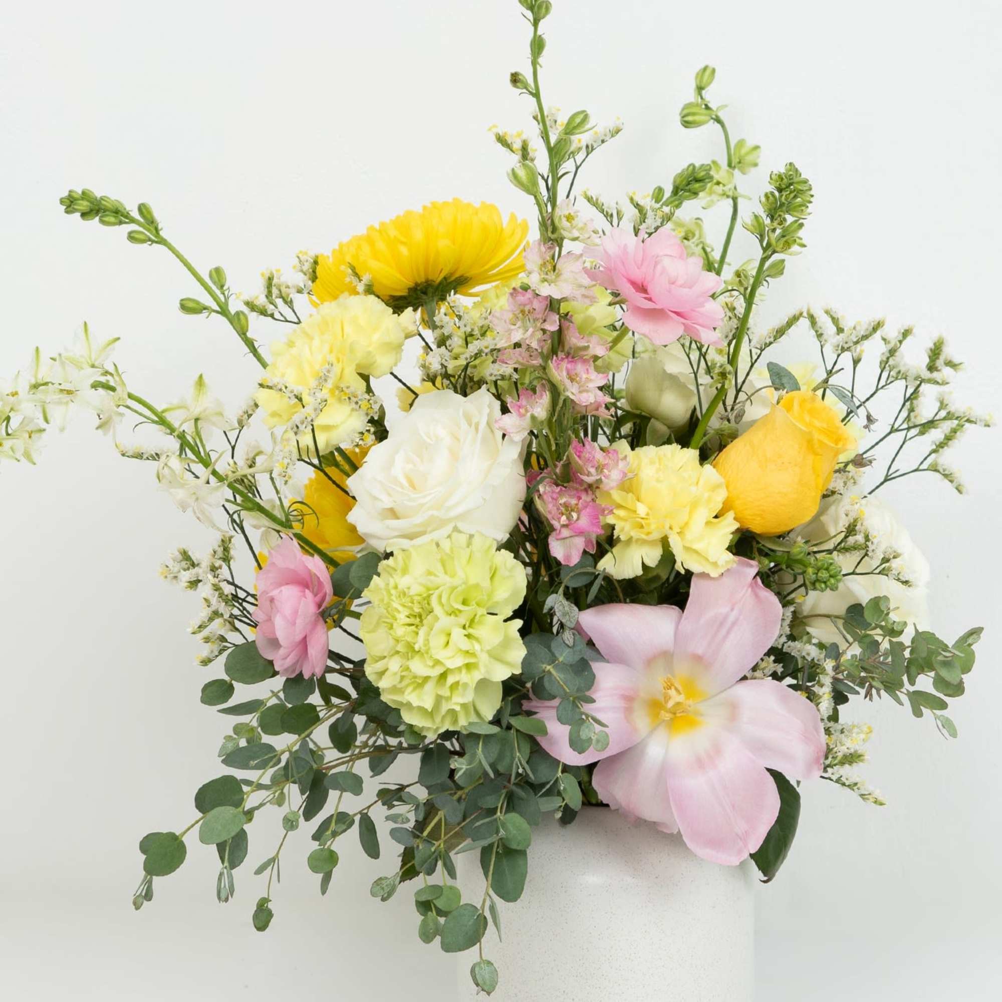 Pastel yellow, pink, and white mixed flower arrangement in a white ceramic vase