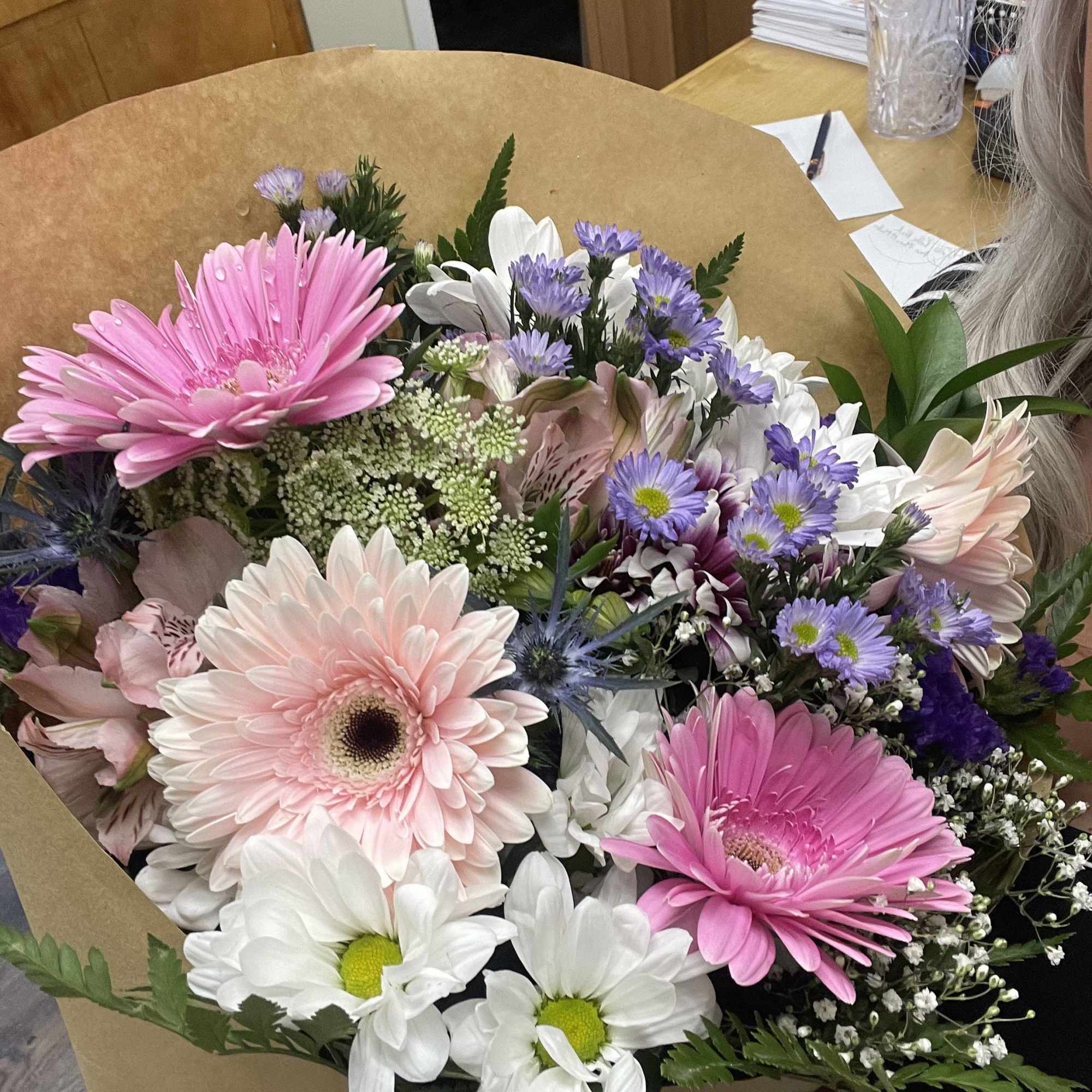 Bouquet of pink gerbera daisies, white daisies, and purple filler flowers wrapped in brown paper