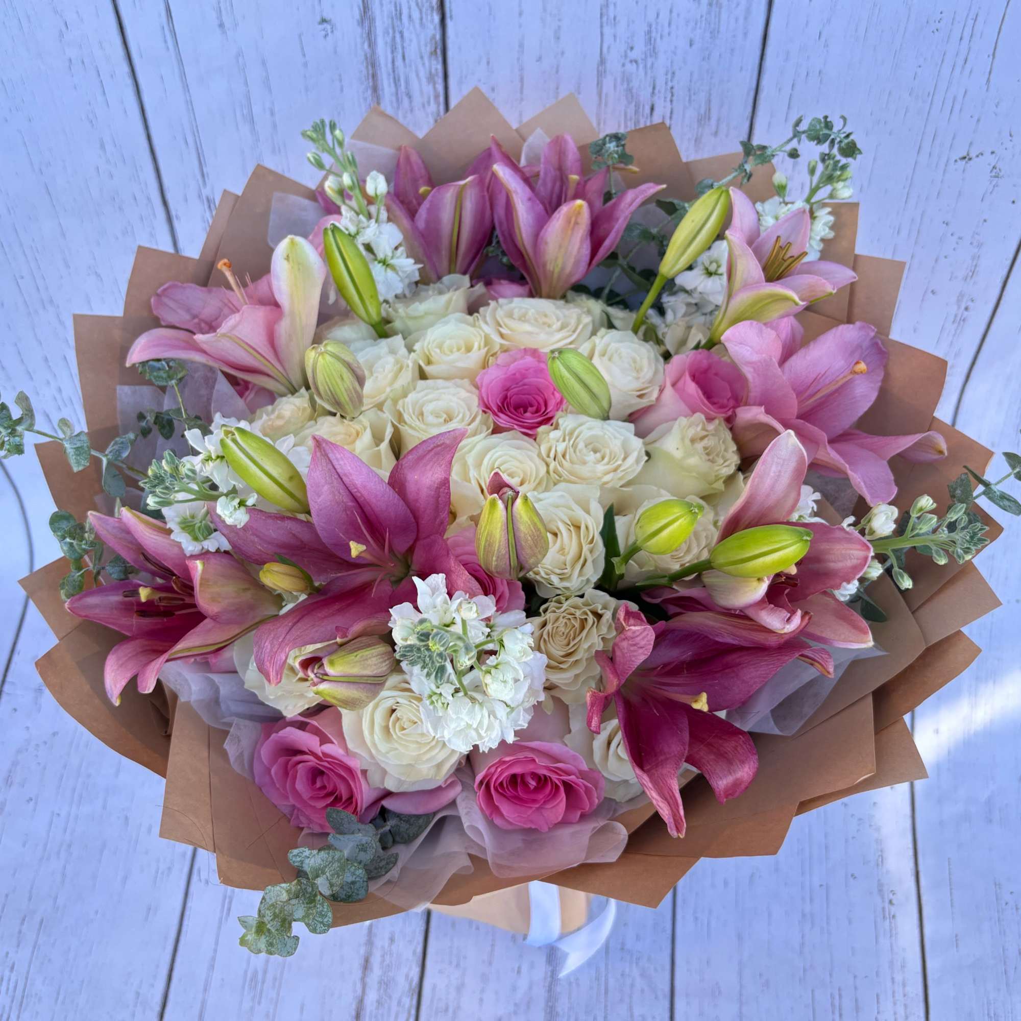 Bouquet of pink lilies and cream roses wrapped in brown paper