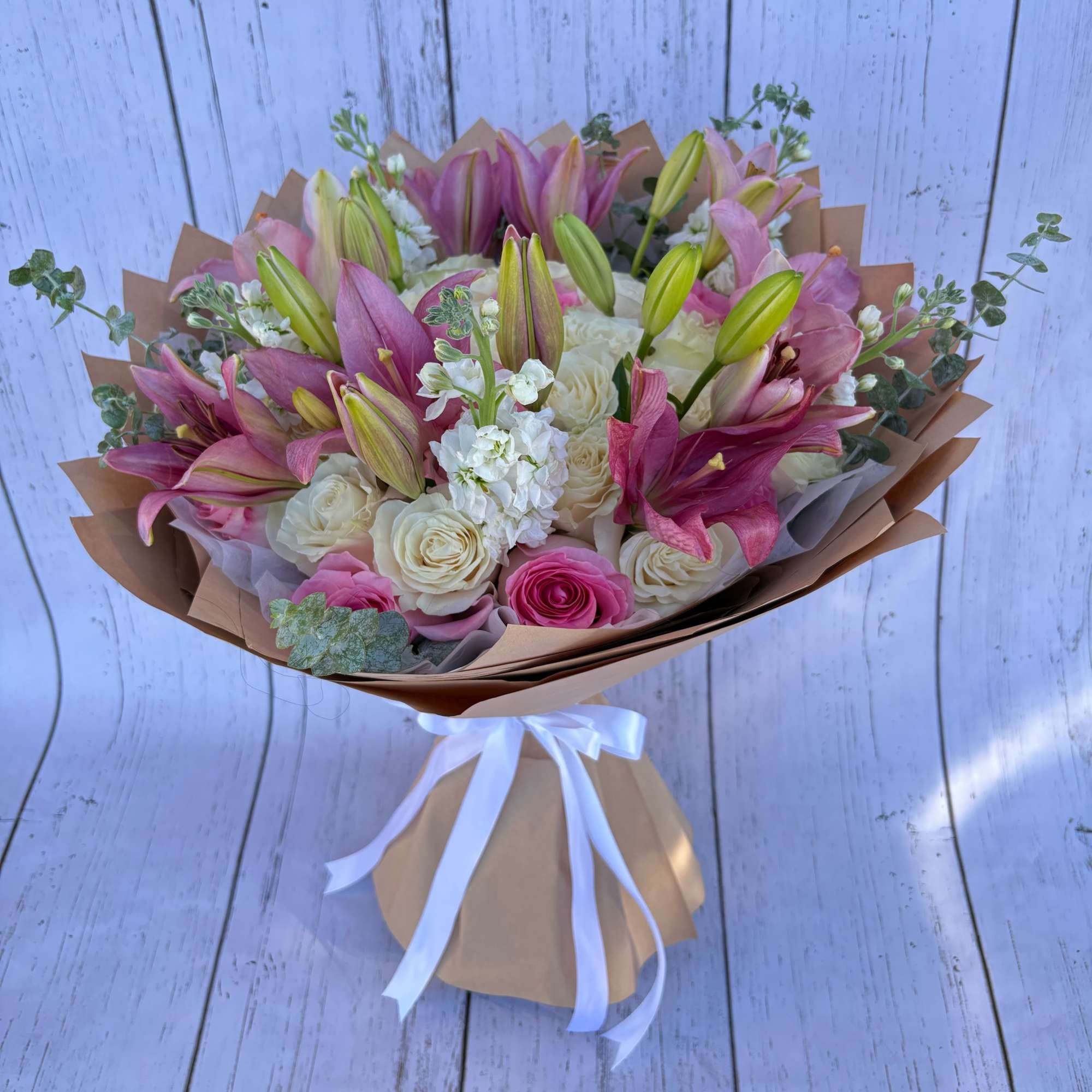Bouquet of pink lilies and cream roses wrapped in brown paper