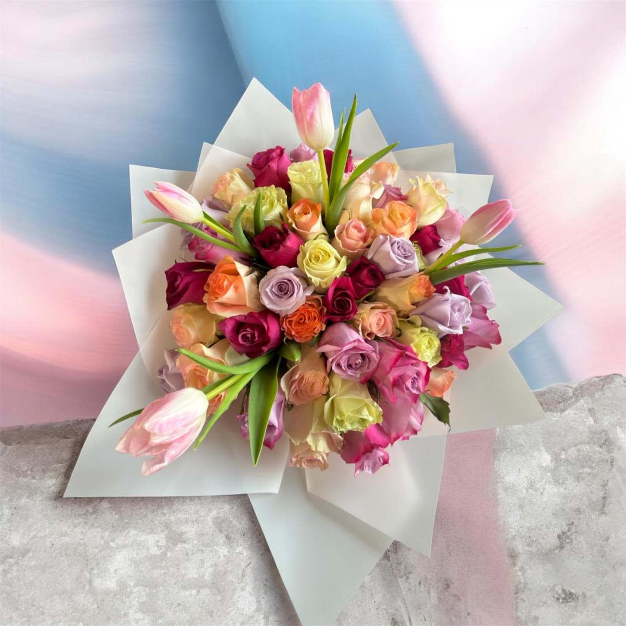 Bouquet of multicolored roses with pink tulips in white wrap
