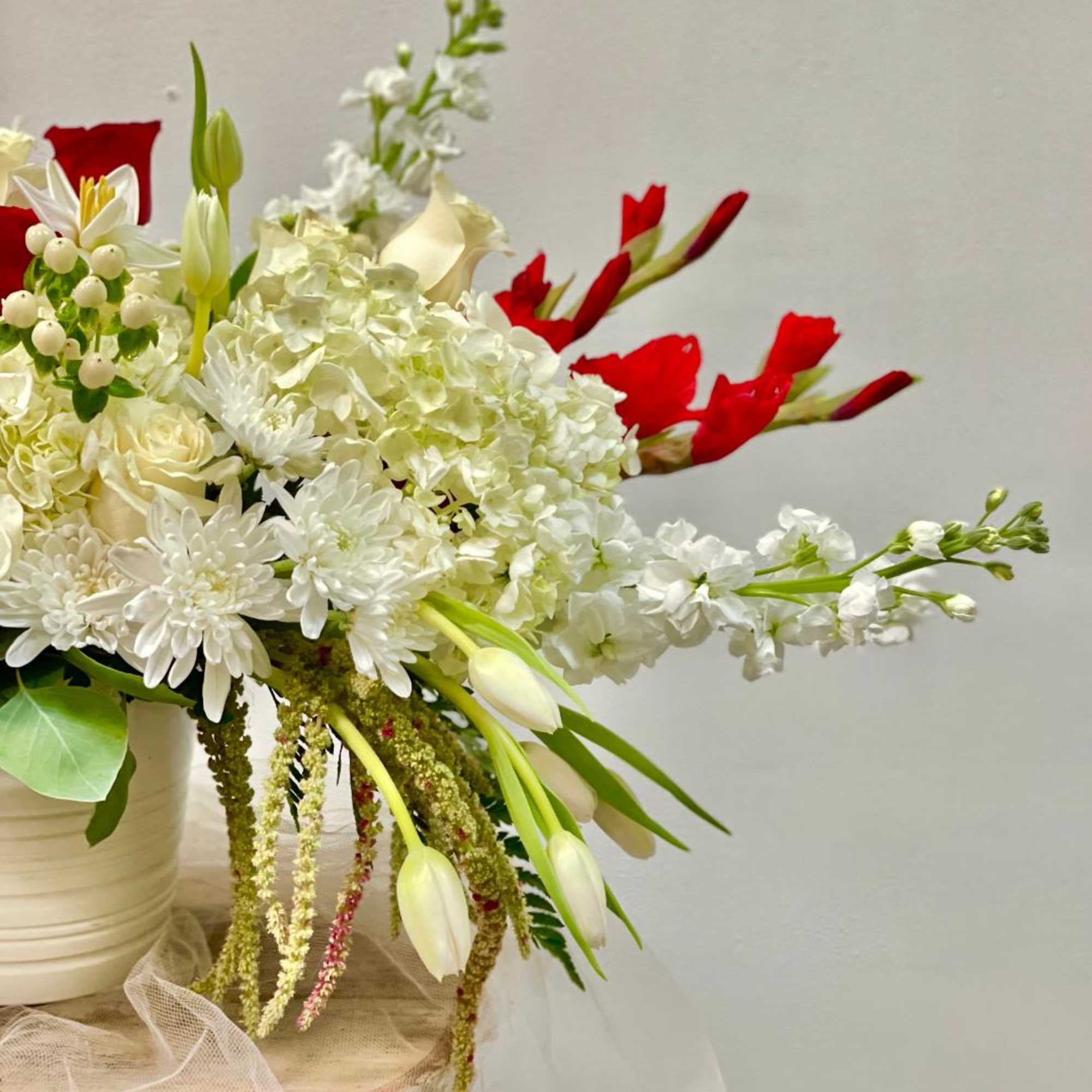 White floral arrangement with red accents in a cream vase
