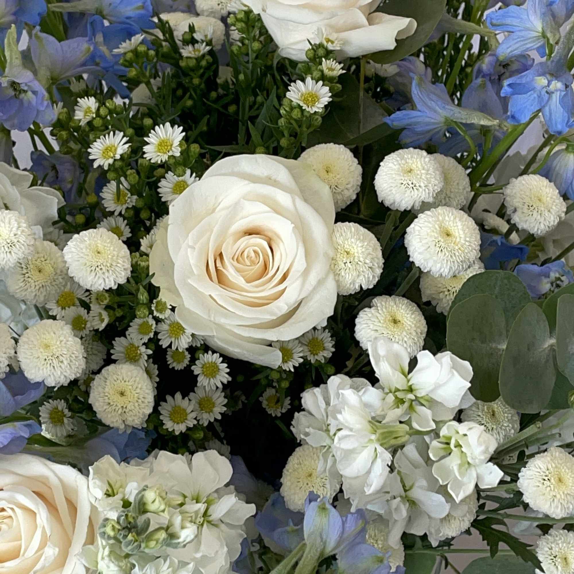 Bouquet of white roses and blue flowers in a glass vase