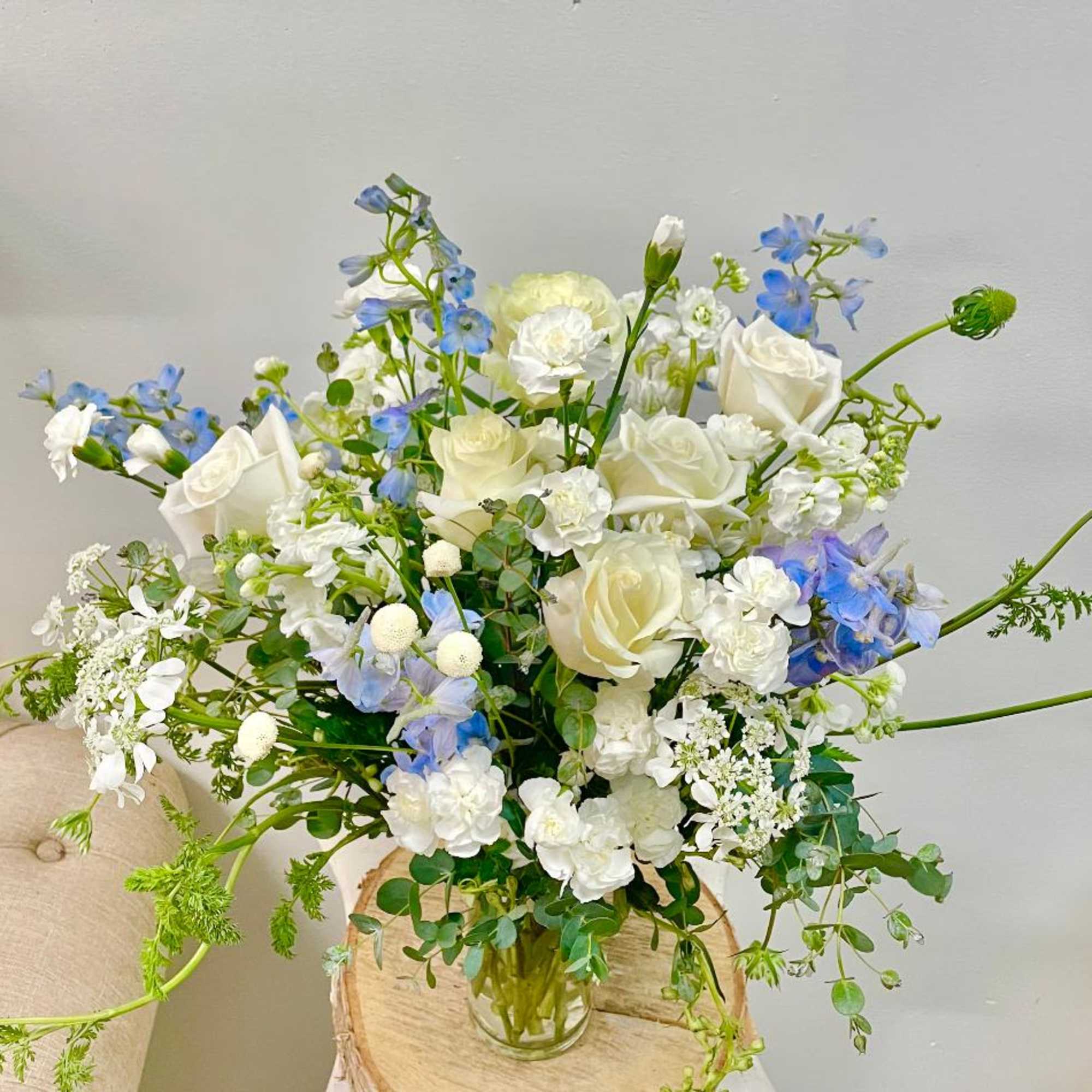 White roses and blue flowers arranged in a clear glass vase