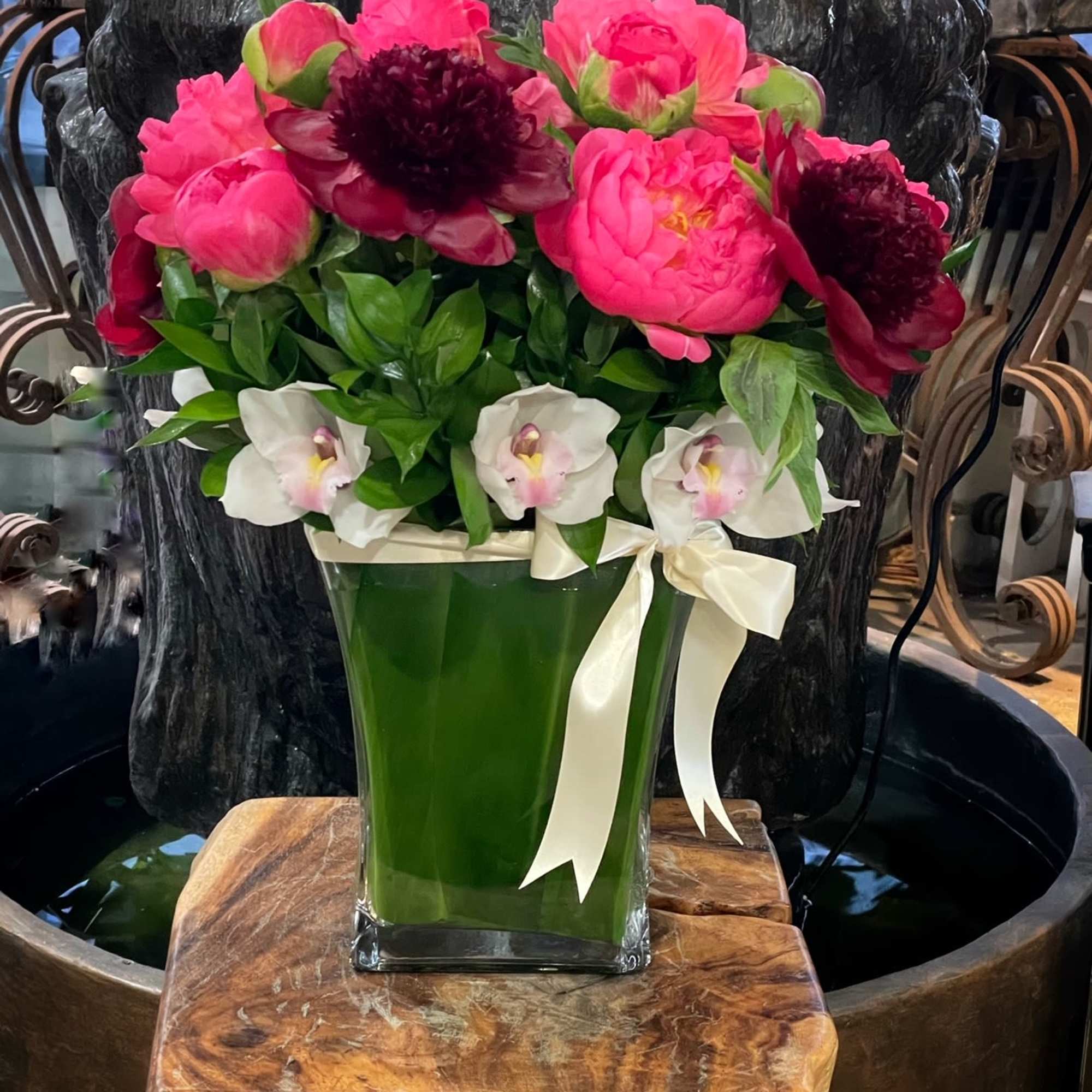 Pink peonies and white orchids in a green glass vase with a ribbon