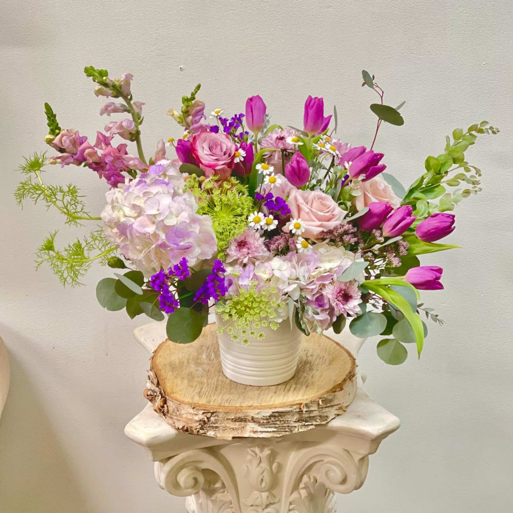 Mixed pink and purple flowers in a white vase on a wood slice
