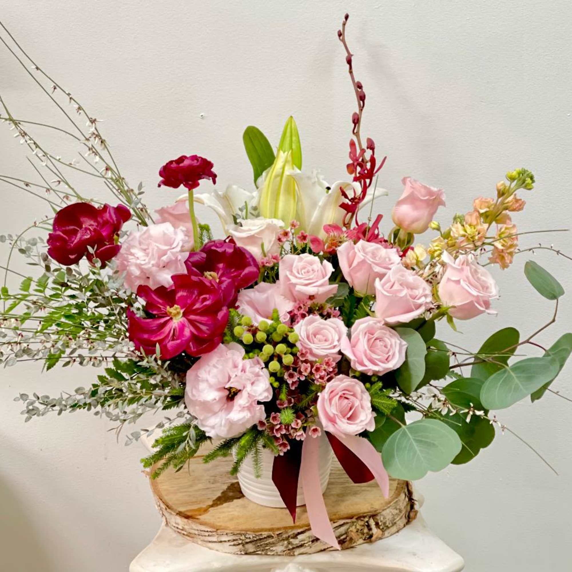Pink and red floral arrangement in a white container with lilies and roses