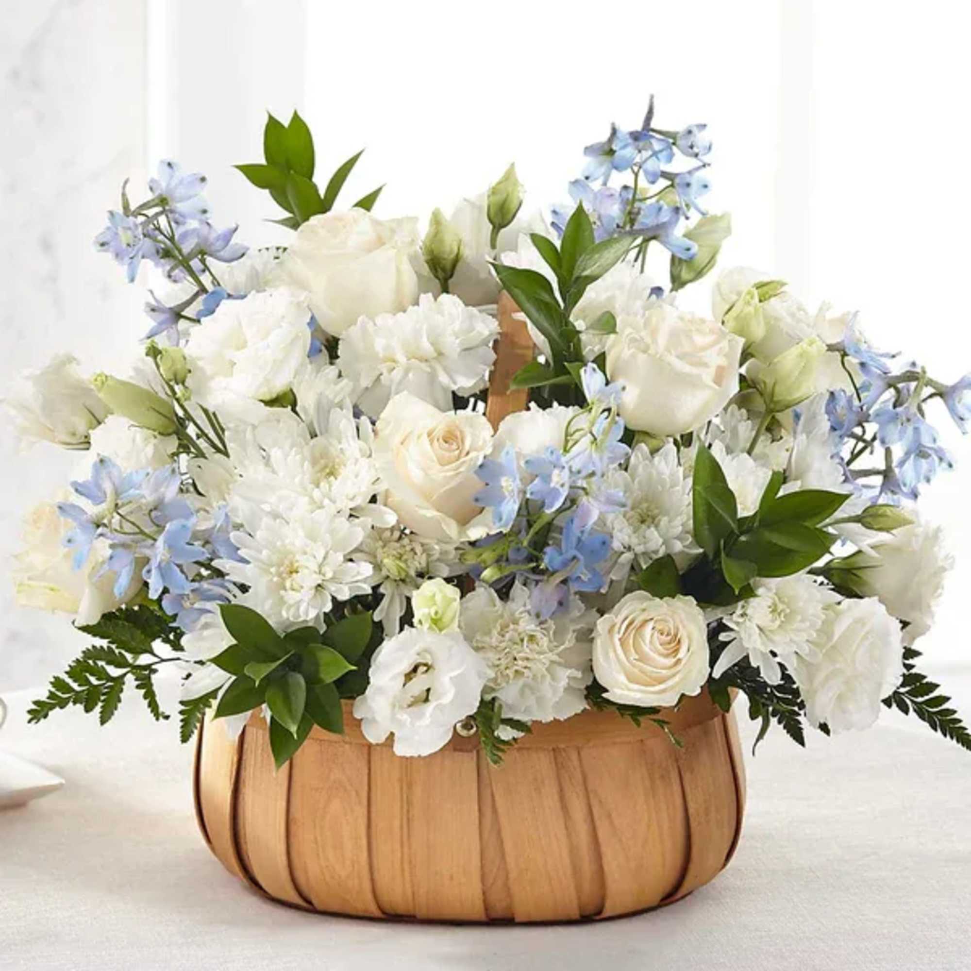 White floral arrangement with pale blue flowers in a wooden basket