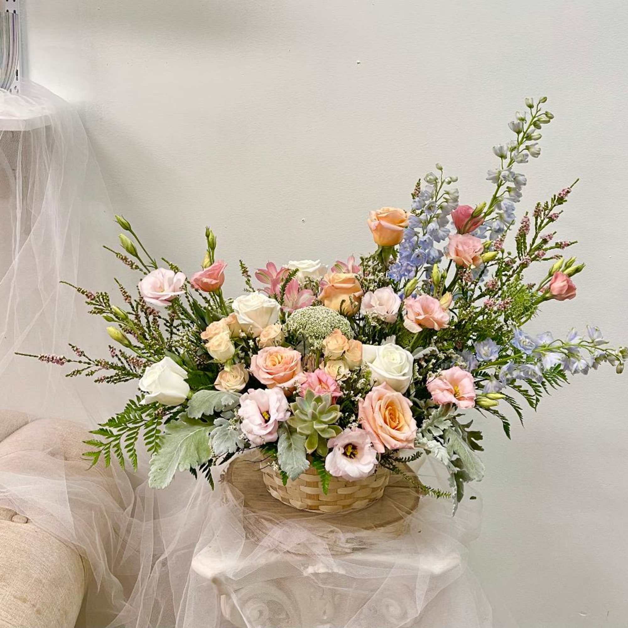 Pastel bouquet of roses, lisianthus, and blue delphinium in a woven basket