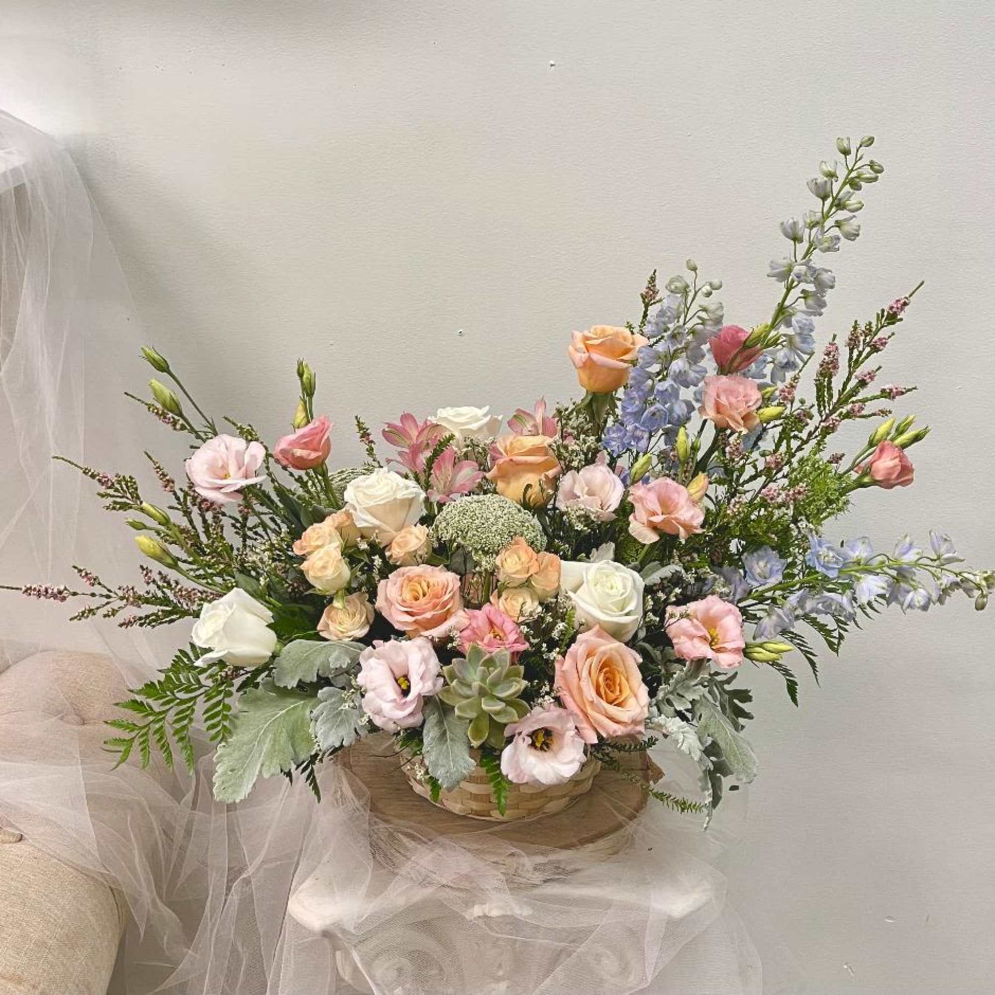 Pastel floral arrangement in a woven basket with roses and tall blue blooms