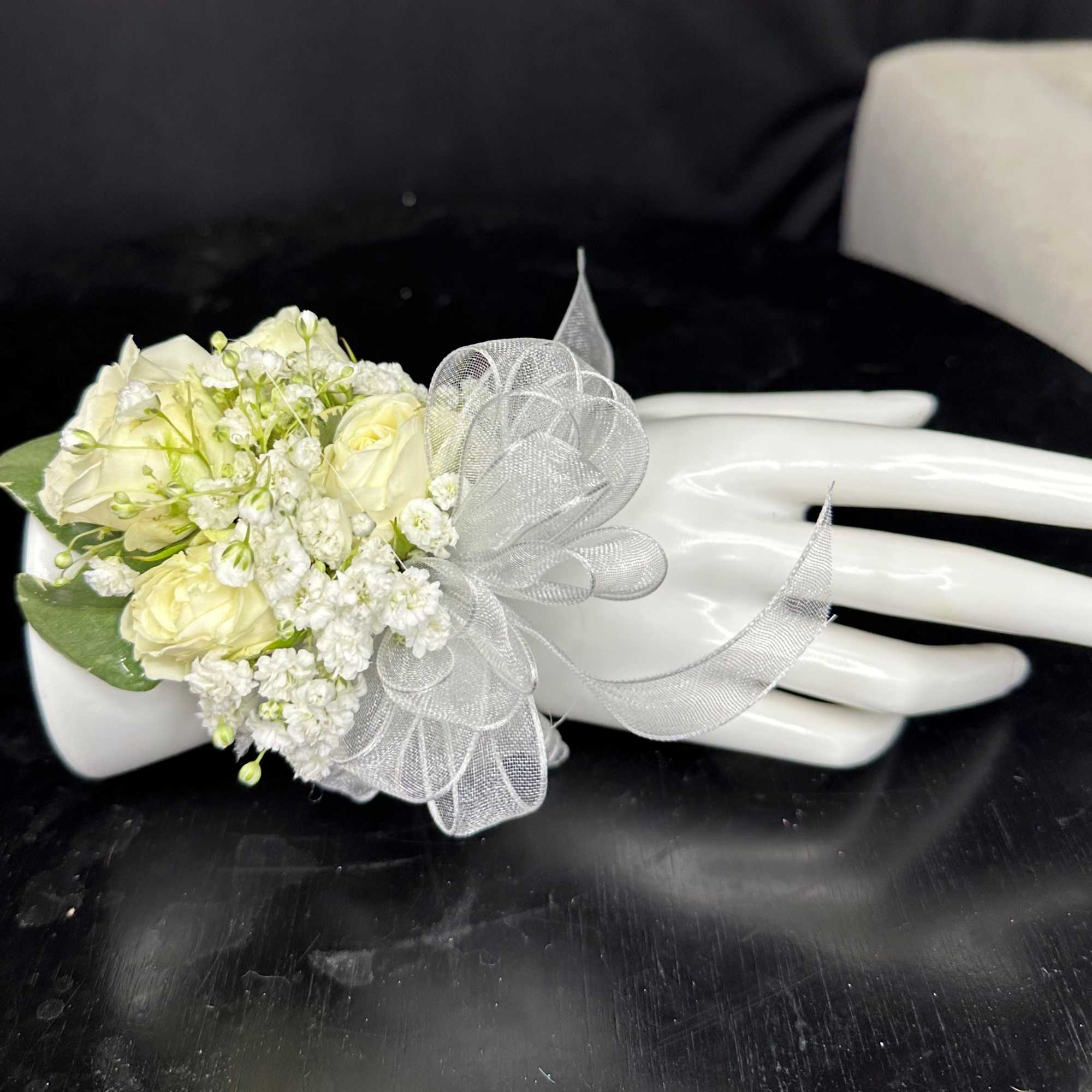 White rose corsage with a sheer silver ribbon on a mannequin hand