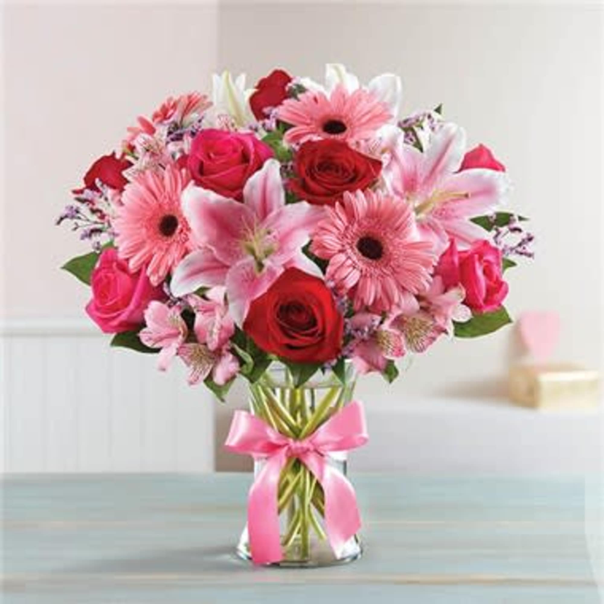Bouquet of pink and red flowers in a glass vase with a pink ribbon